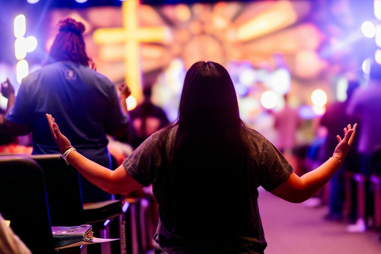 Back view of people engaged in a vibrant religious service with colorful lighting and a cross.
