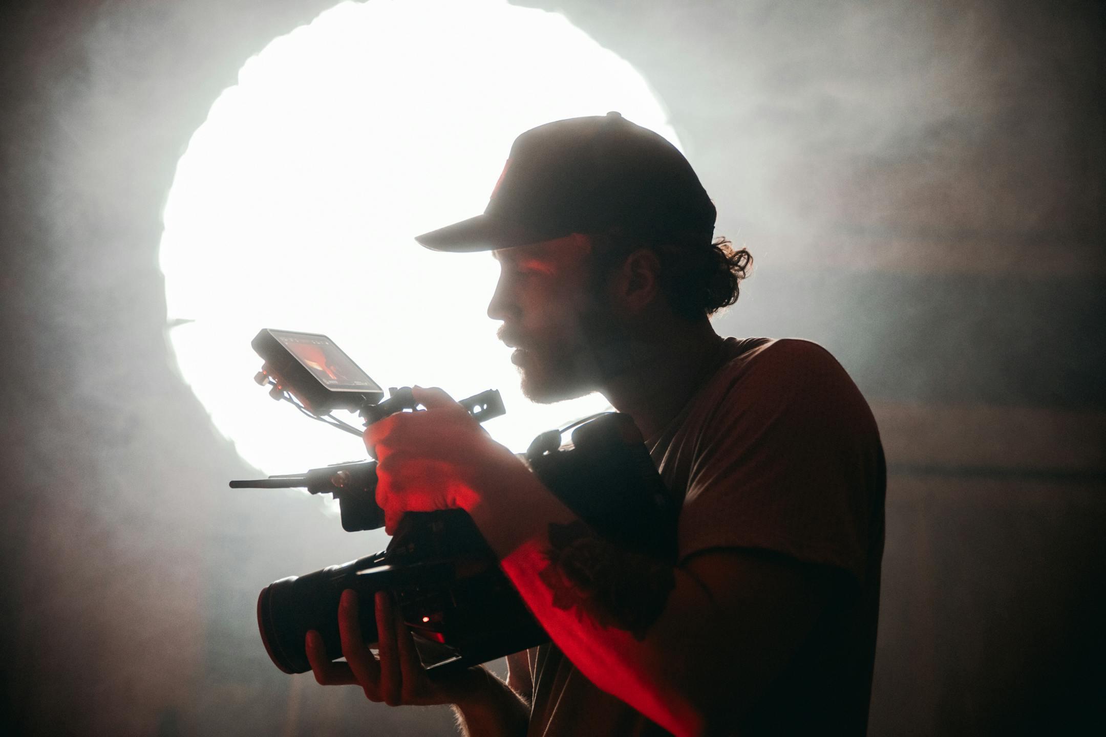 Silhouette of a cinematographer filming with a camera in a smoky setting, dramatic lighting.