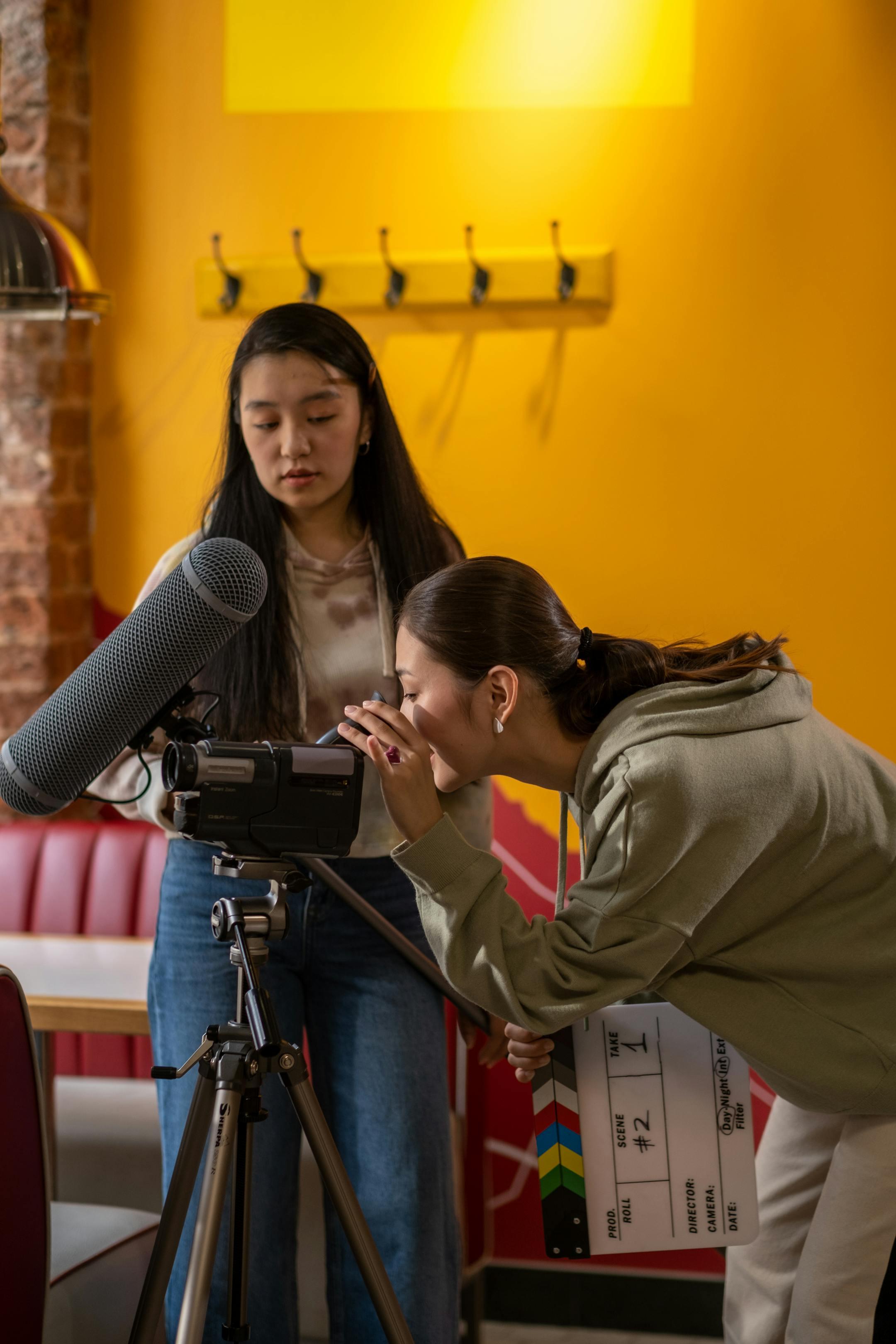 Two young women collaborating on a film set indoors with camera and equipment.