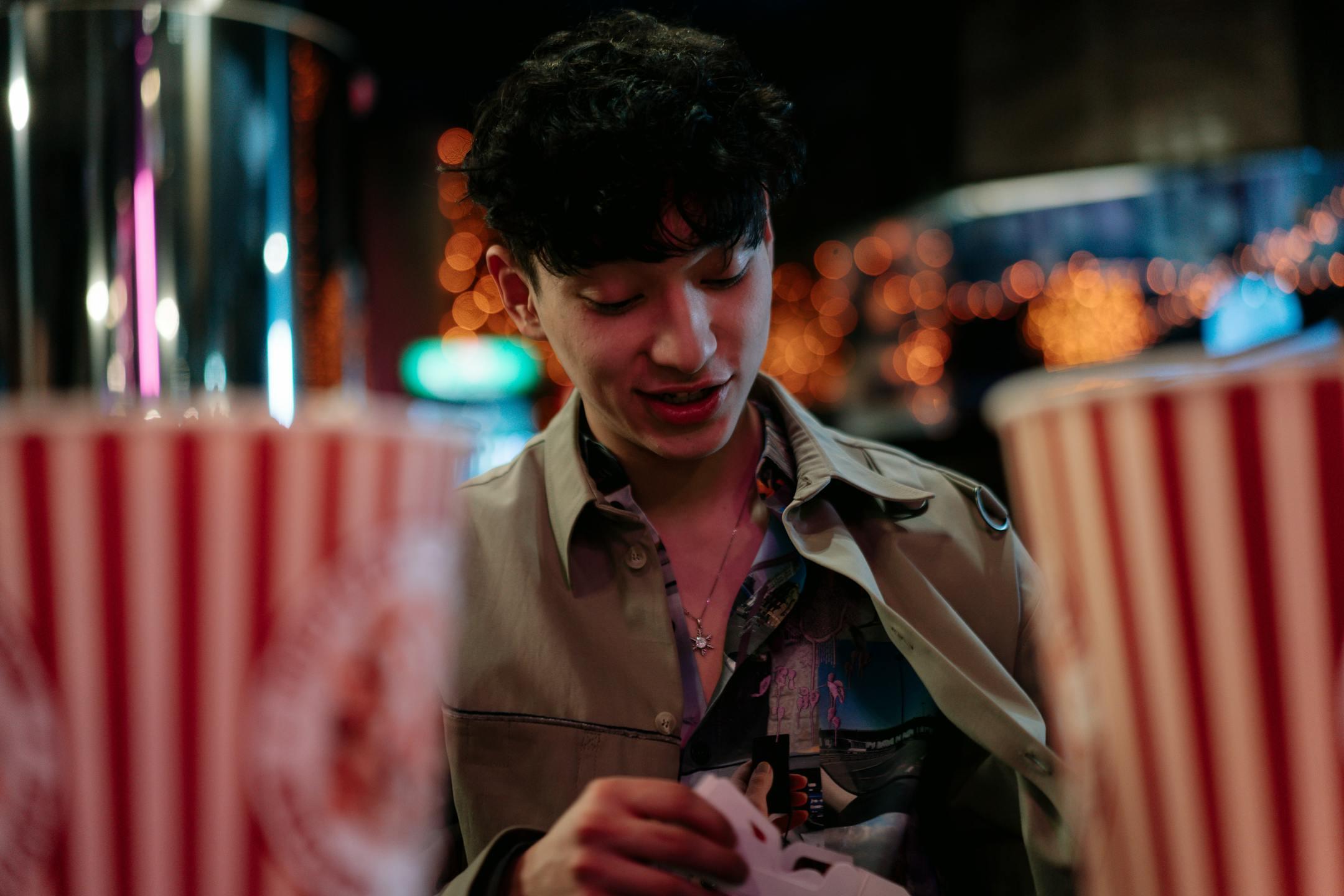 A young man enjoys a night out at the cinema, surrounded by popcorn and dim lights.