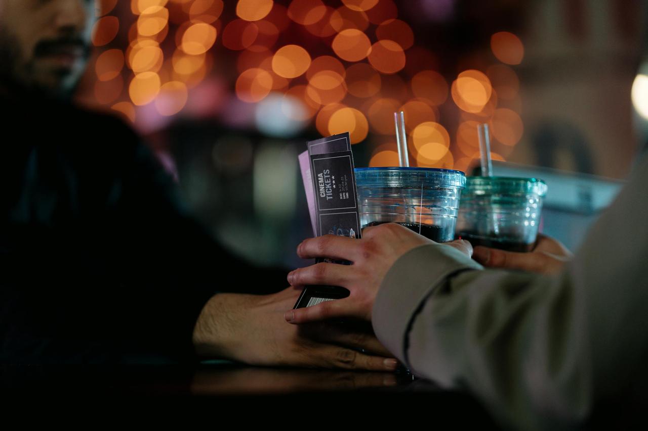 Close-up of hands exchanging cinema tickets and plastic cup drinks with straws.
