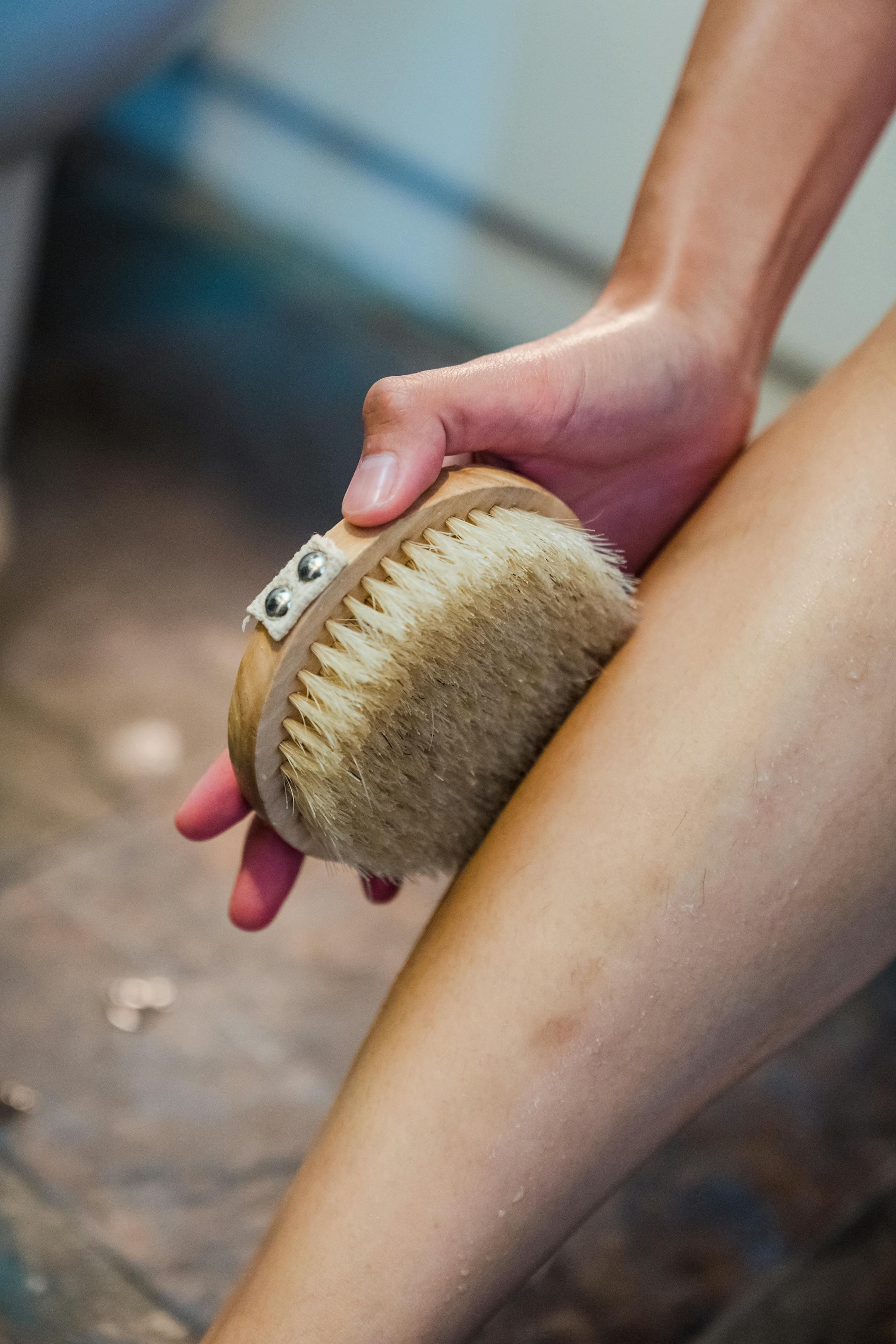 Hand using a body brush on leg for personal hygiene and exfoliation.
