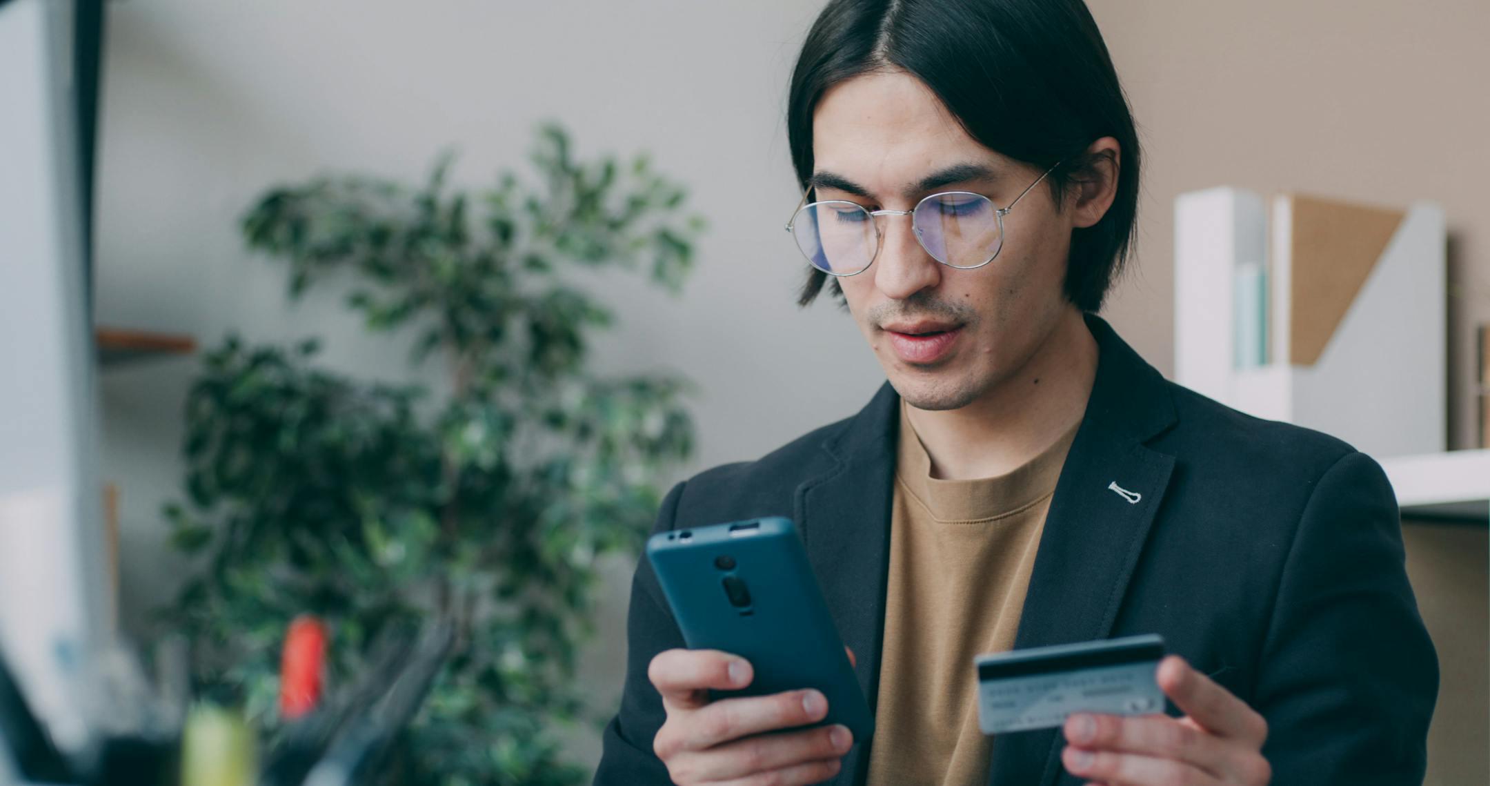 Businessman in office attire using a smartphone and holding a credit card, focusing on online payment process provided by SlidePay.