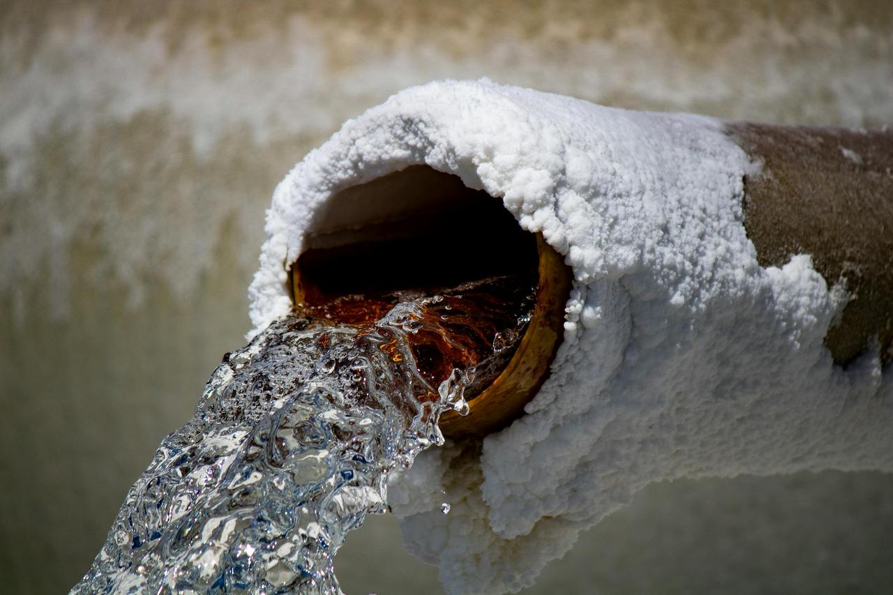 Close-up of water flowing from a rusty pipe with salt deposits, capturing motion and texture.