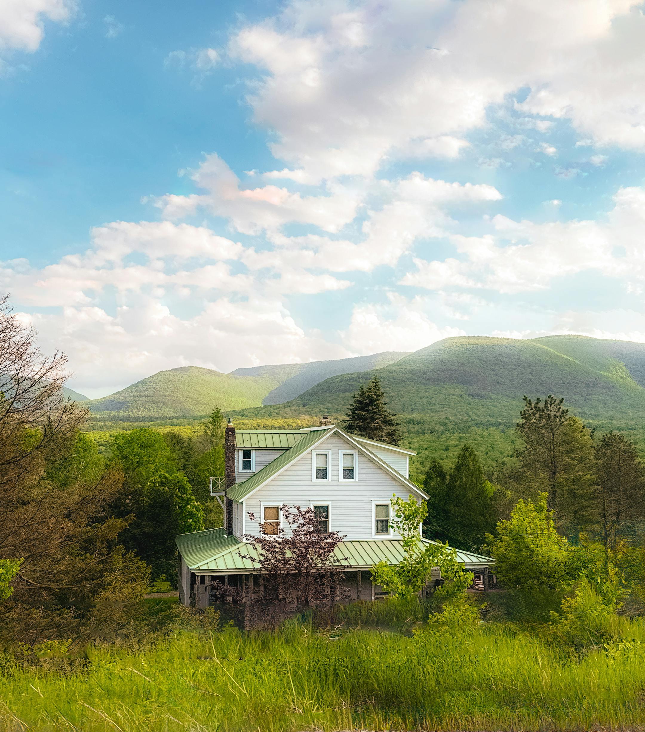 Charming house nestled in a verdant valley with mountain views under a bright sky.
