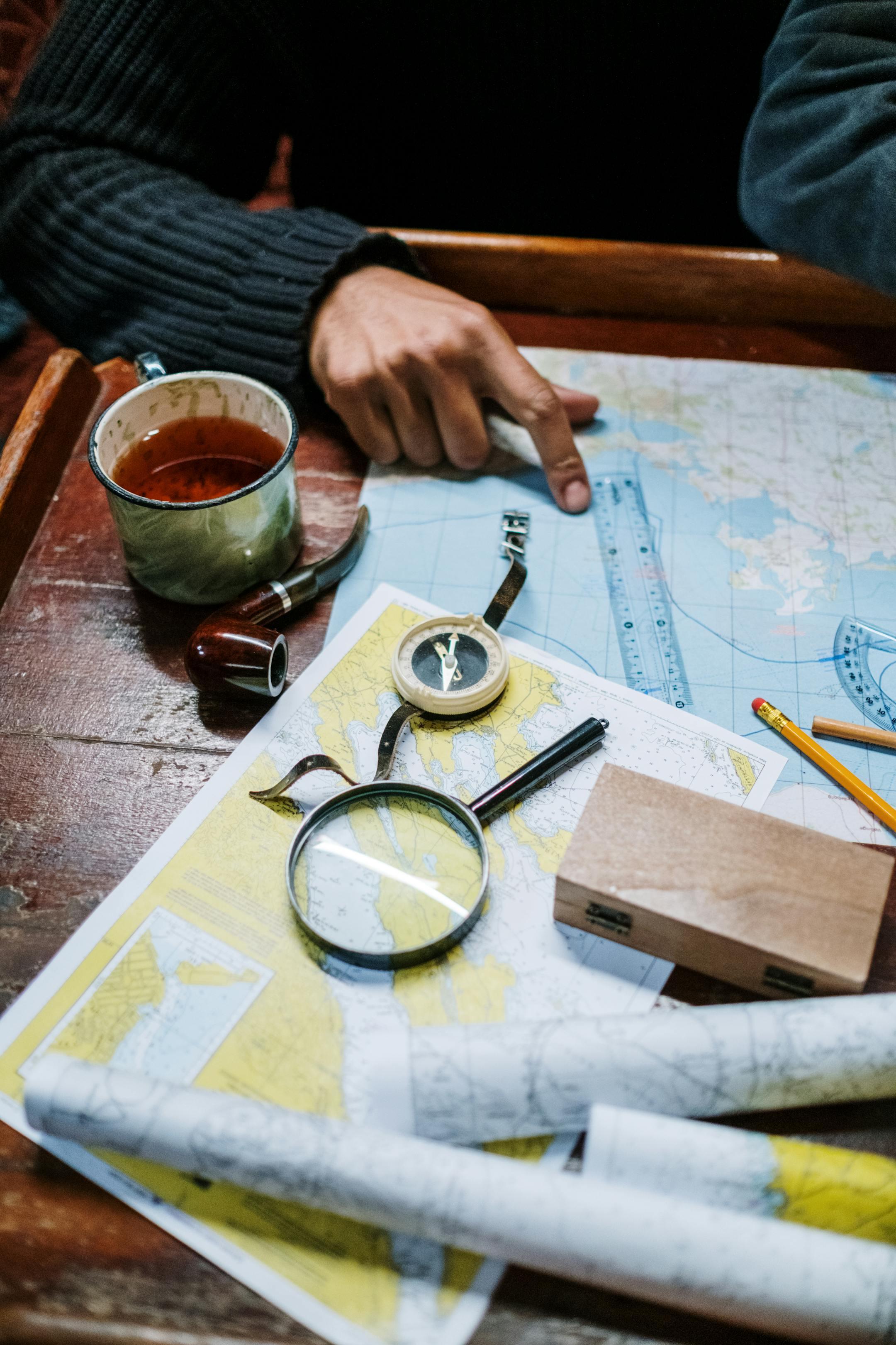 Man planning a journey with nautical maps, compass, and navigational tools on a wooden table.