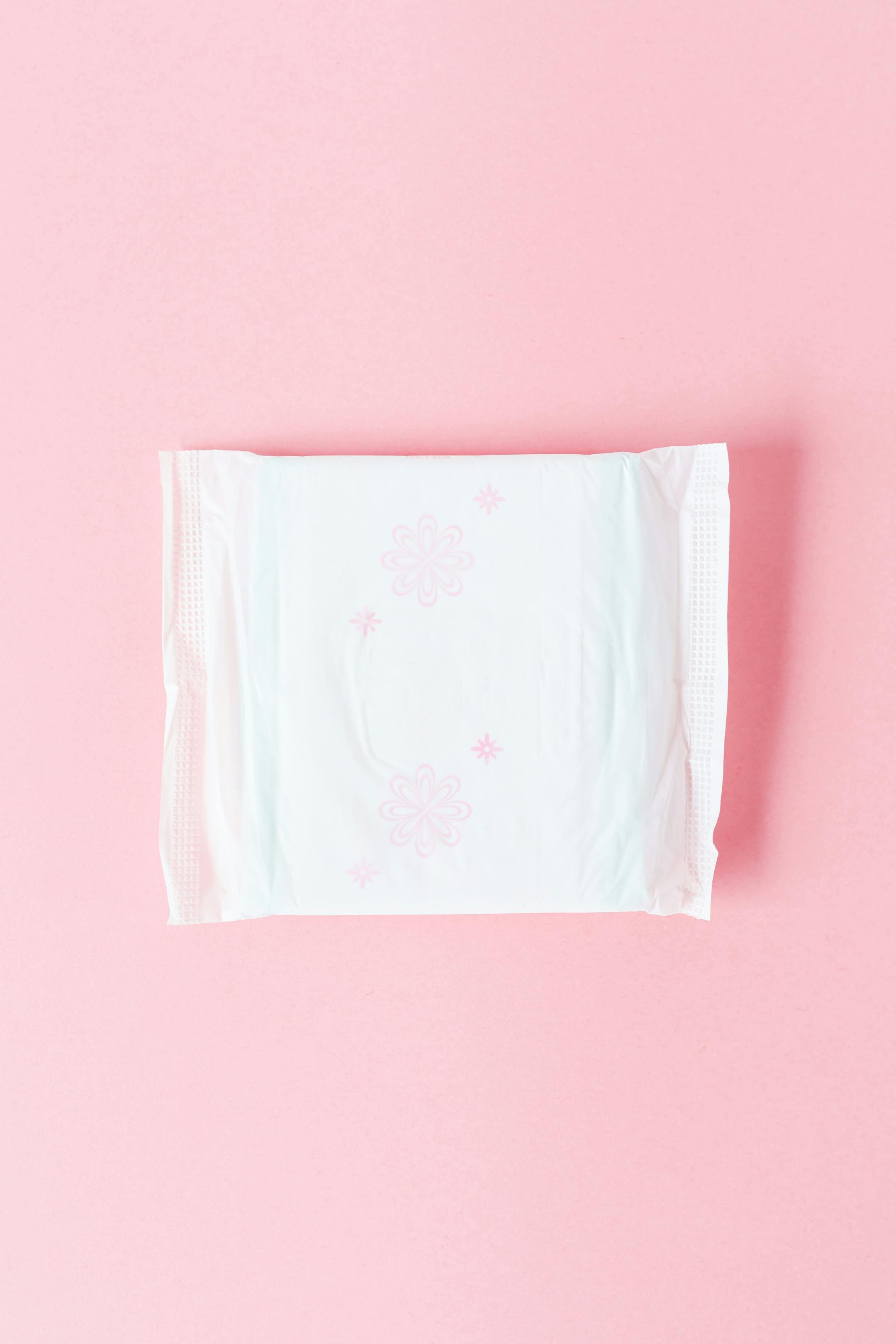 Top view of a feminine hygiene pad on a pastel pink background, ideal for health and wellness topics.
