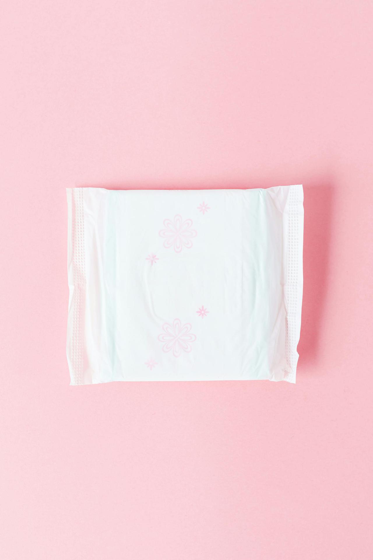 Top view of a feminine hygiene pad on a pastel pink background, ideal for health and wellness topics.