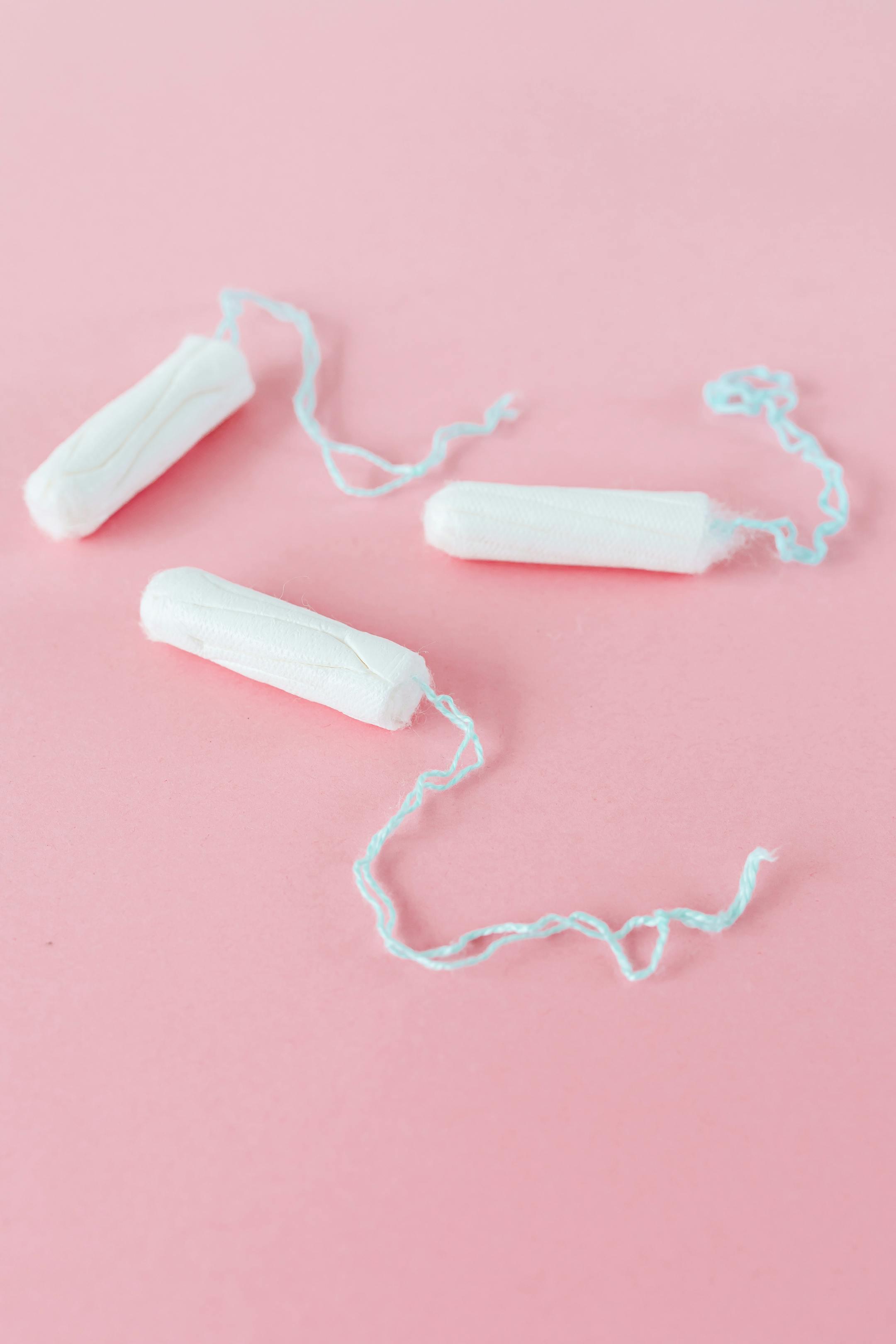 Three white tampons laid on a plain pink background, showcasing feminine care.