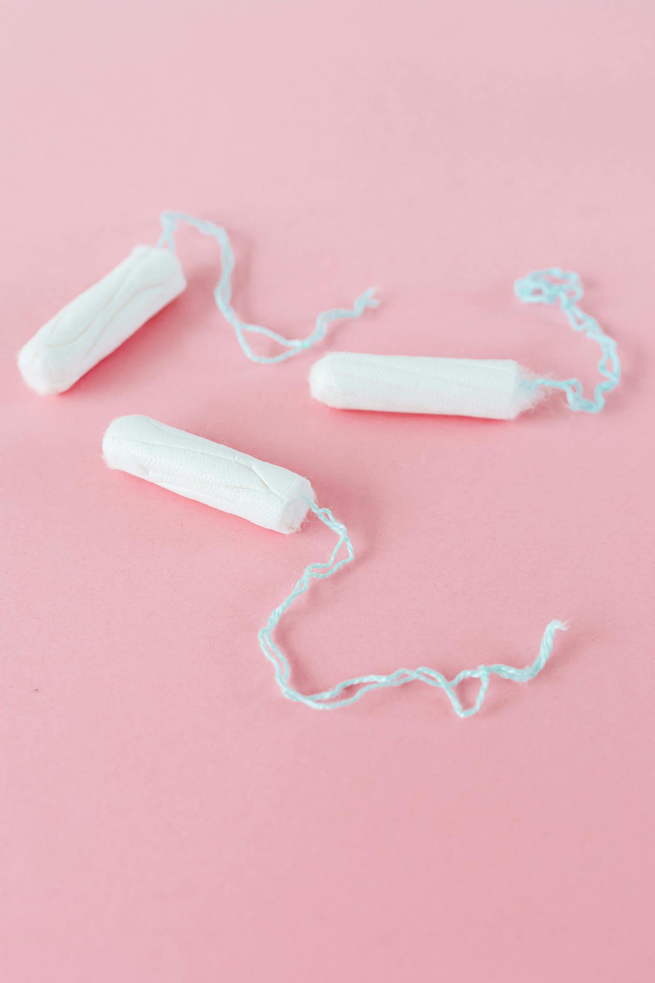 Three white tampons laid on a plain pink background, showcasing feminine care.