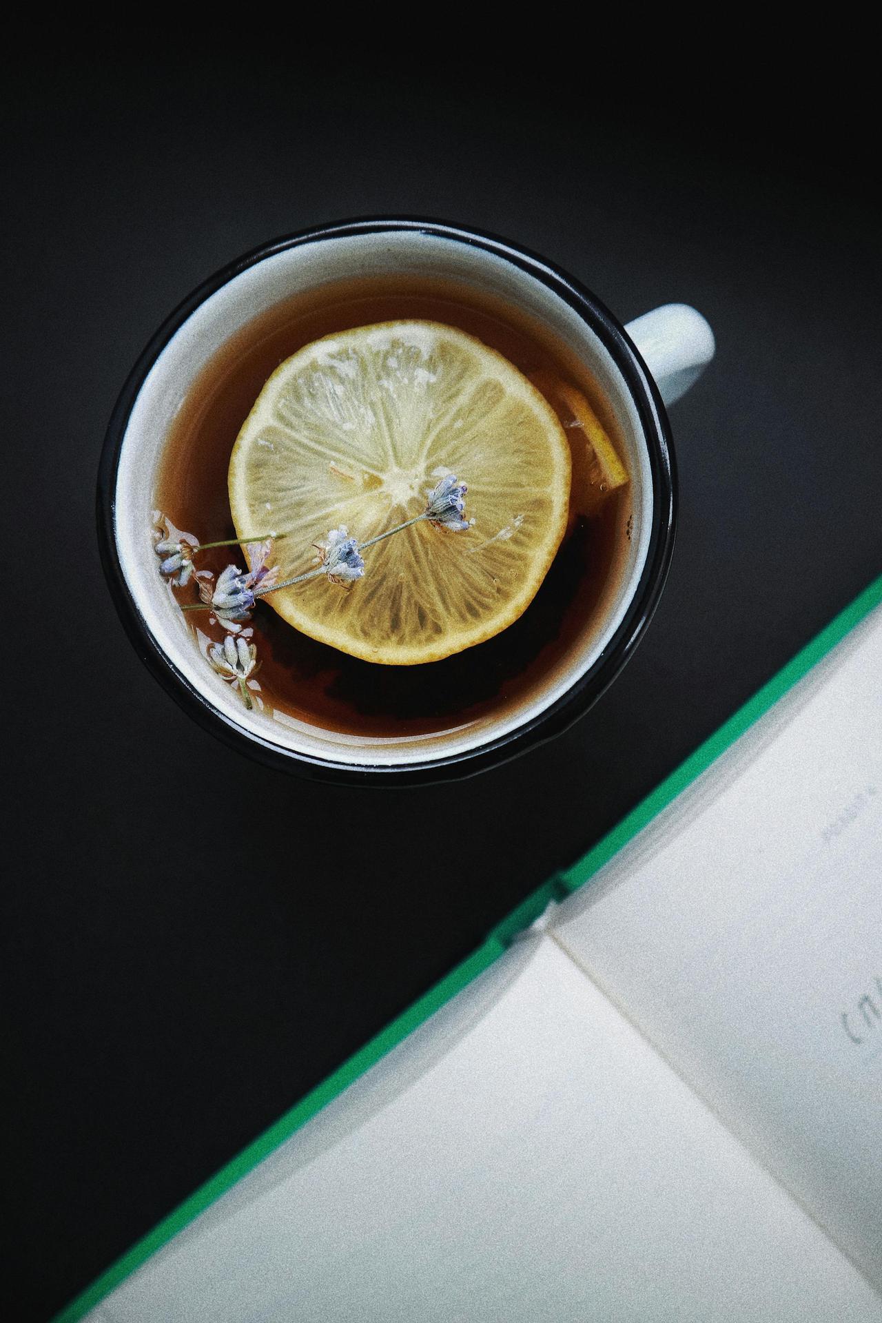 A close-up view of a lemon herbal tea with lavender flowers and an open book in the background. Perfect cozy moment indoors.