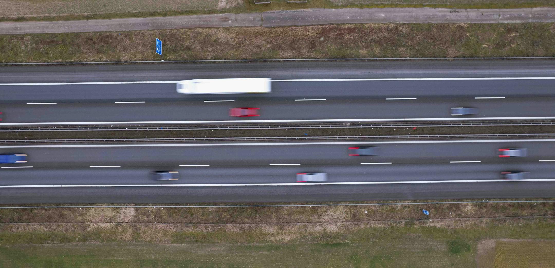 Captured from above, this image portrays the dynamic flow of traffic on a highway. Vehicles blur into streaks of color, illustrating the pace of life on the road. The patterns of the lanes and the sense of movement offer a glimpse into daily commutes and the arteries of transportation.