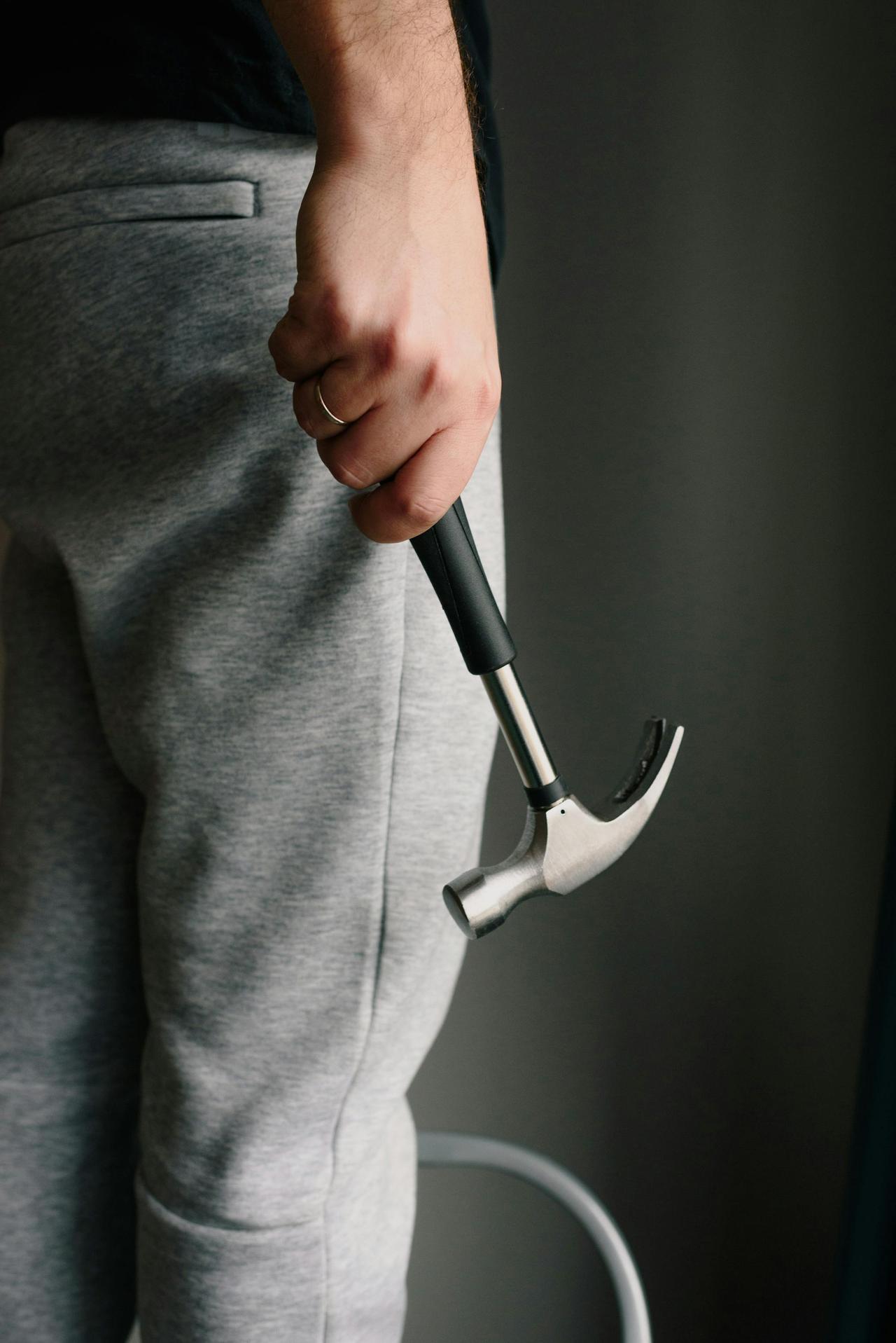 Crop unrecognizable male in casual clothes holding metal hammer with rubber handle in room