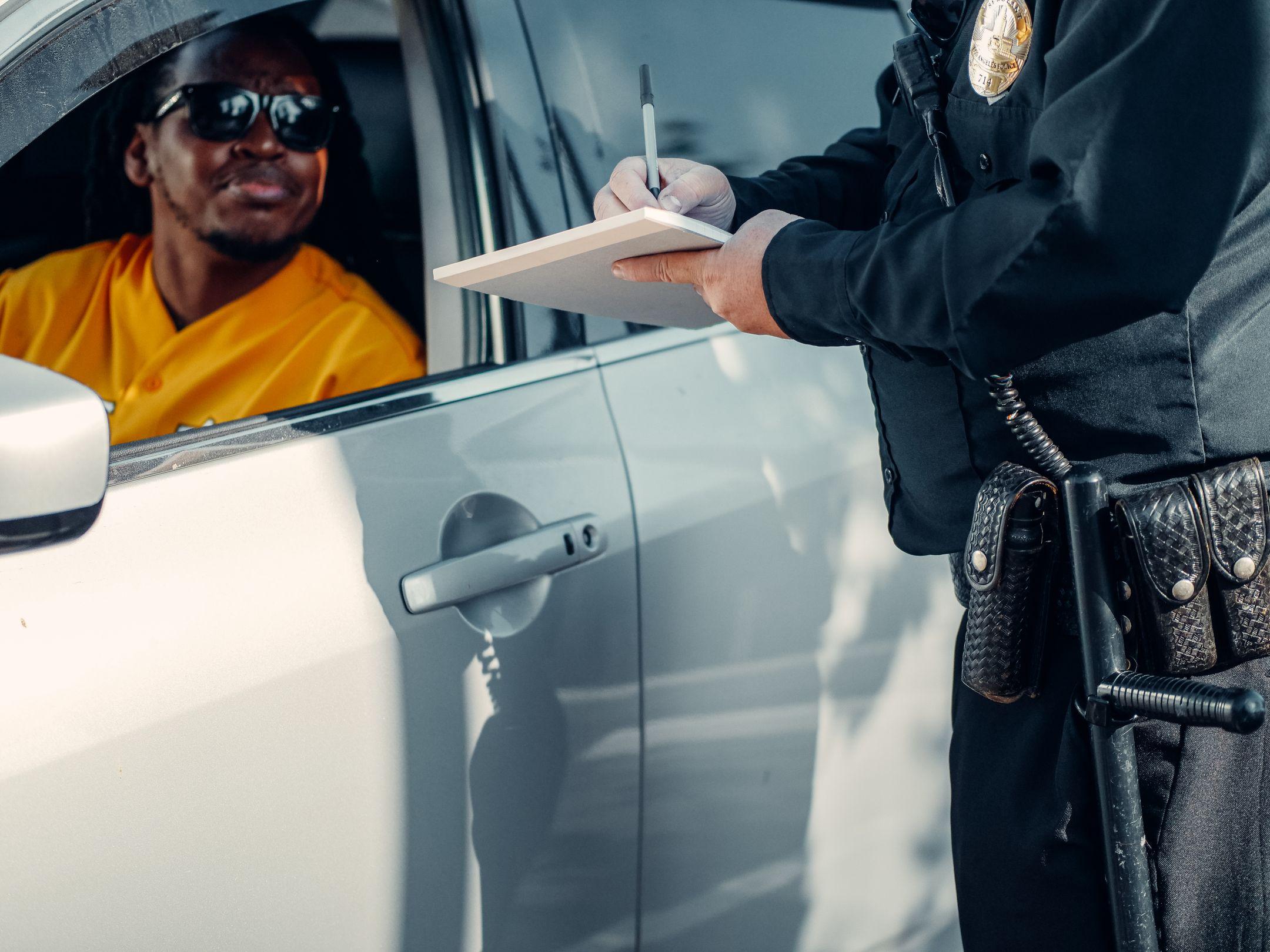 A police officer writes a ticket for a driver in a car during a roadside stop.