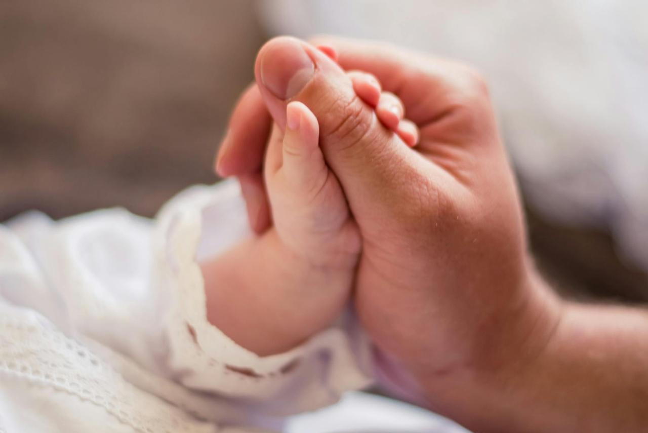 Close-up of an adult hand holding a baby's hand, symbolizing love and care.