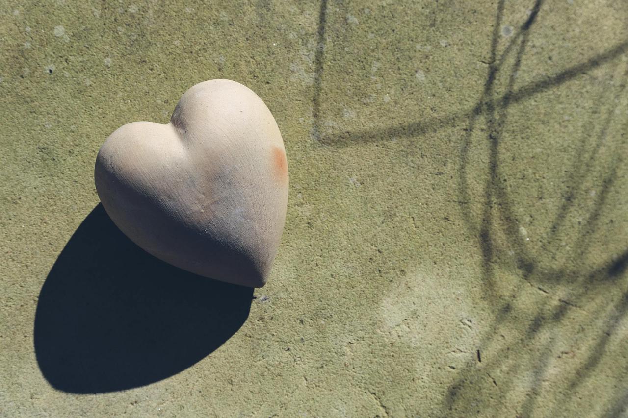 A heart-shaped terra cotta object casting shadows in bright sunlight on a textured surface.