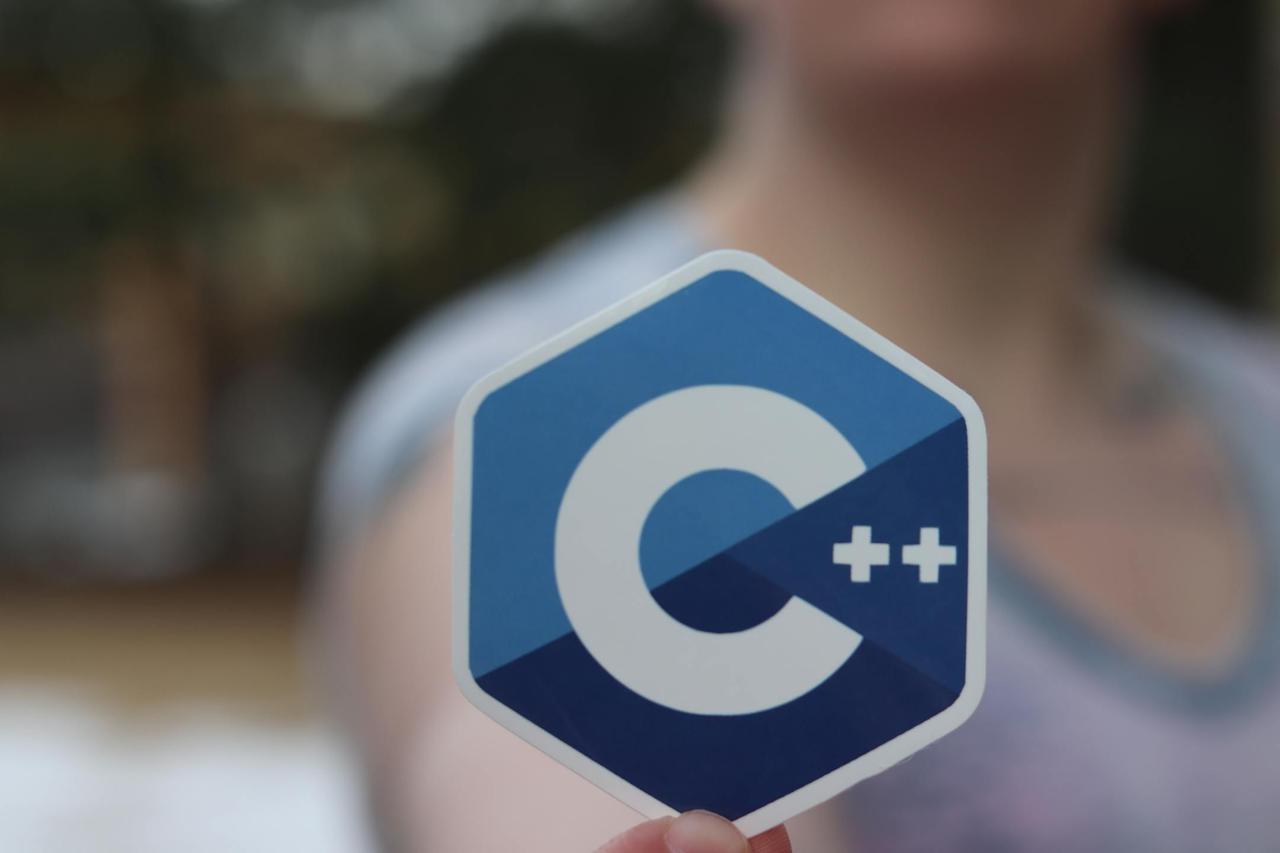 Close-up of person holding a C++ logo sticker, blurred background.