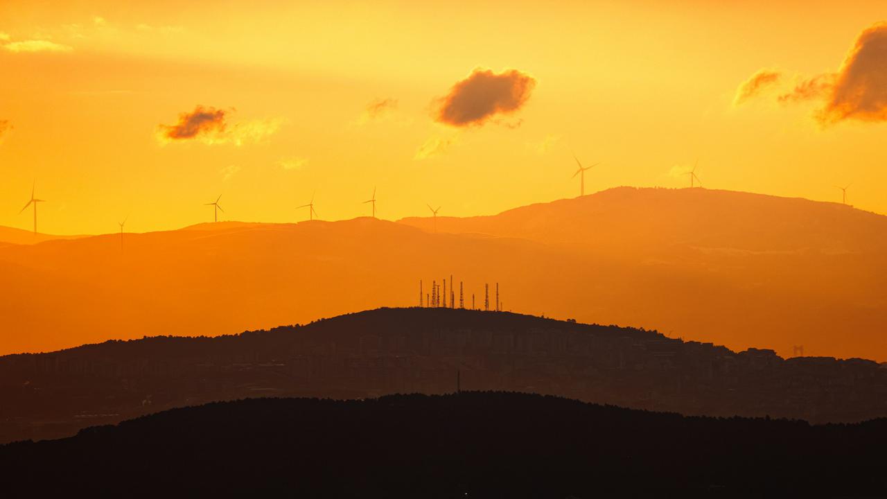 A landscape with wind turbines set against layered mountains, with the city visible in the distance