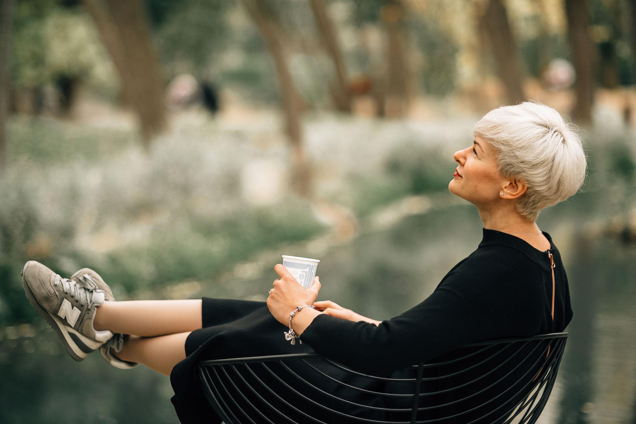 A woman sits contemplatively in a chair with a glass of water in her hand