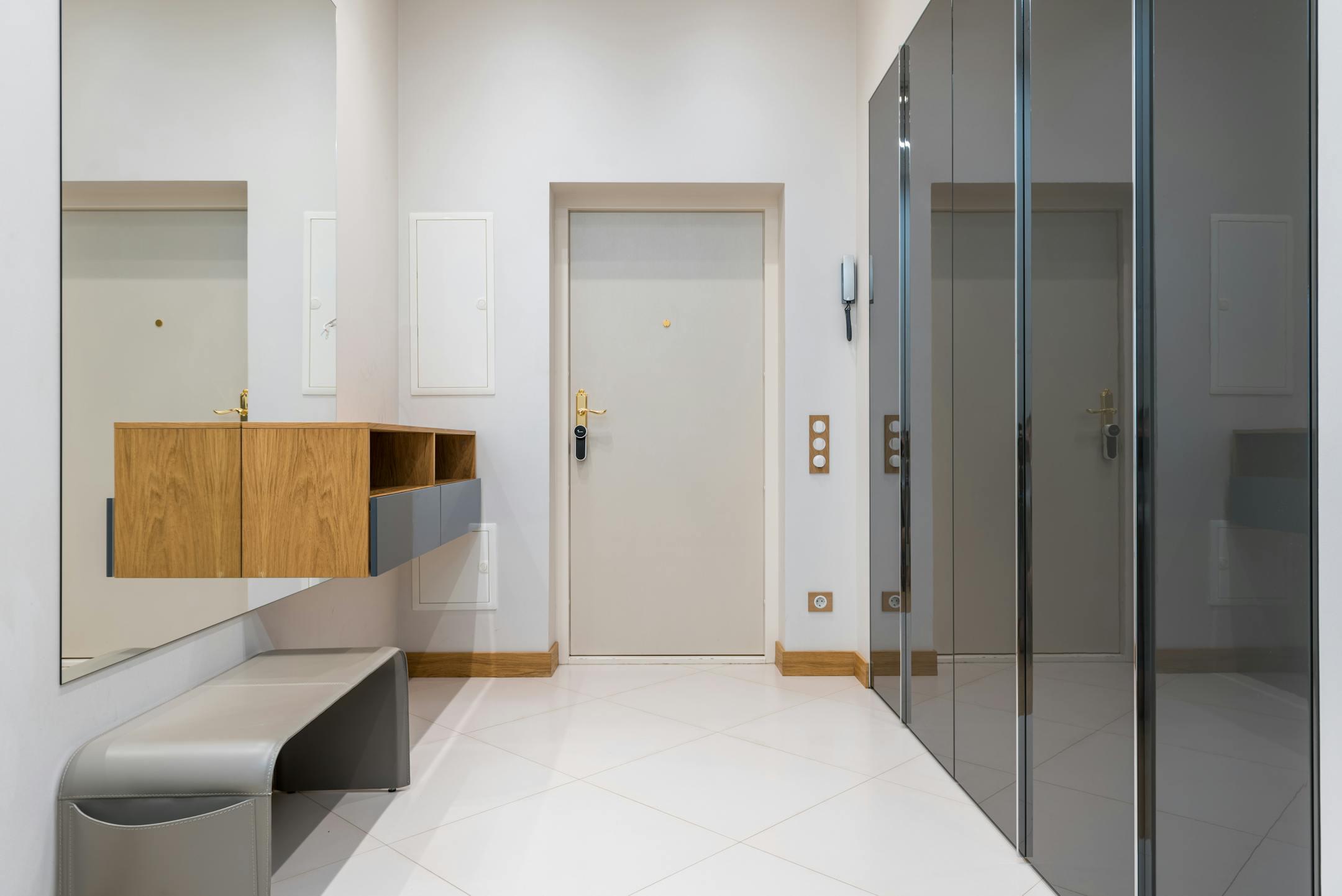 Wooden shelf with bench placed in front of wardrobe with mirrored doors in corridor of modern apartment