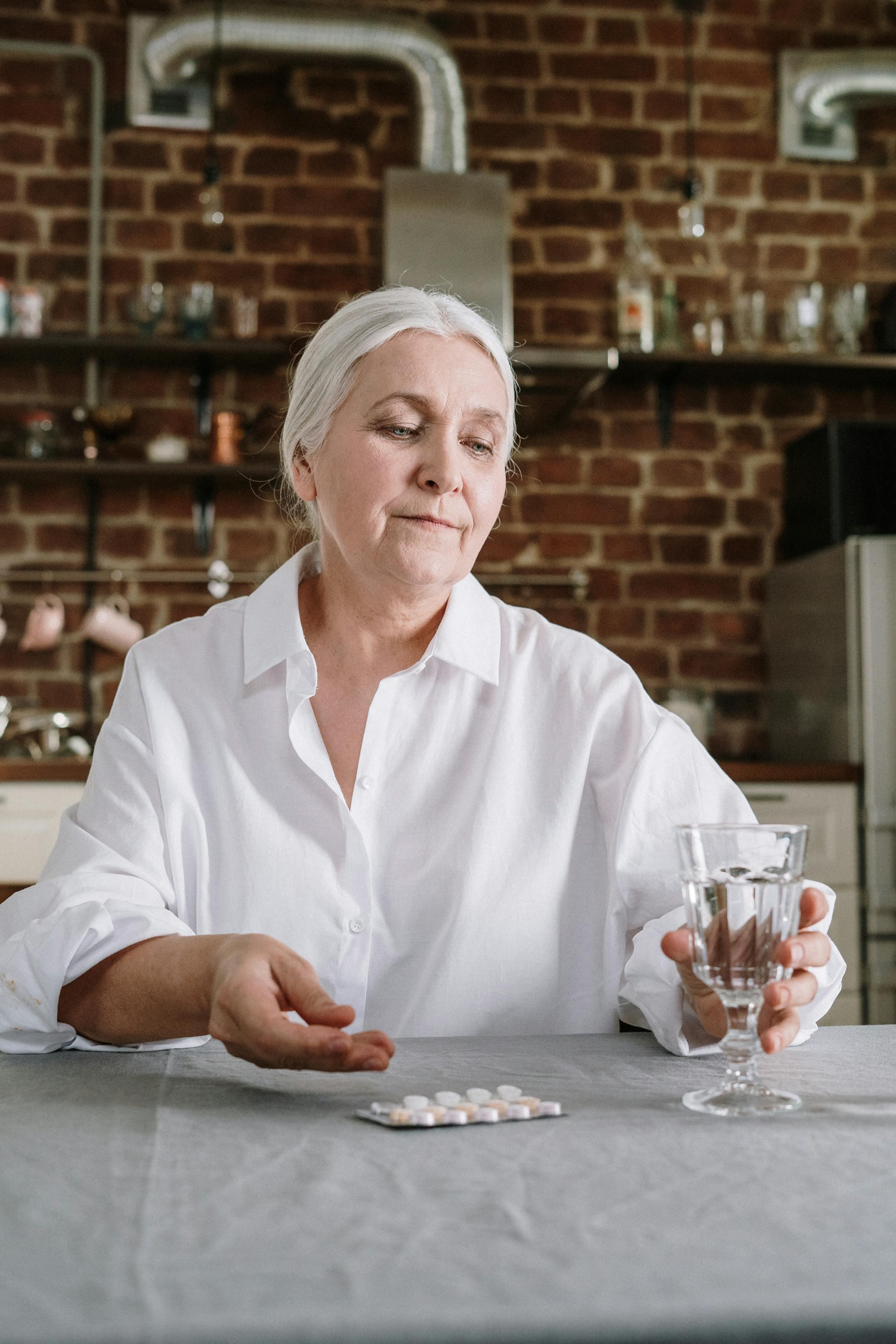 Senior woman at home taking pills with a glass of water.