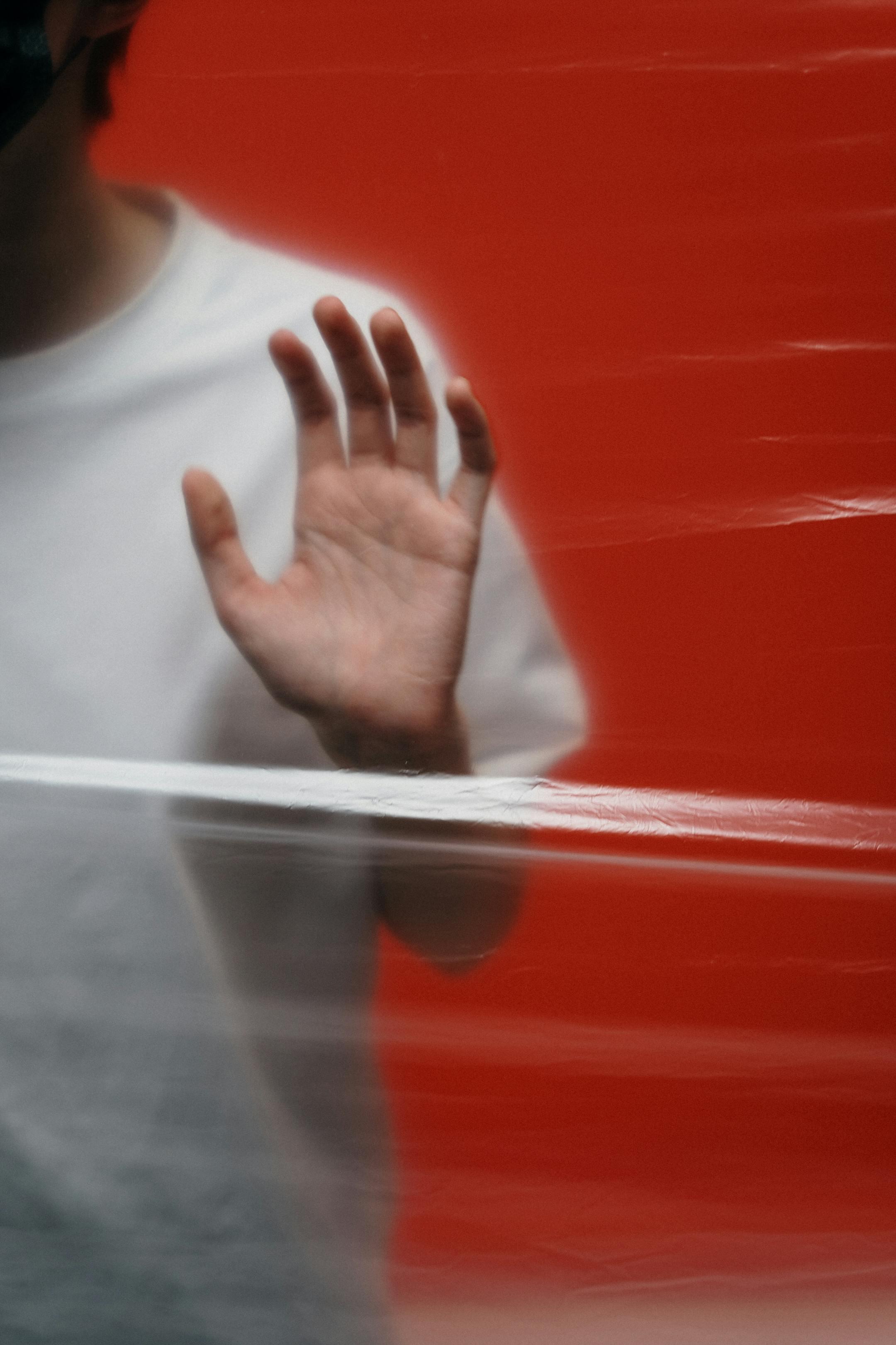 A blurred hand reaching out against a red backdrop symbolizing isolation.