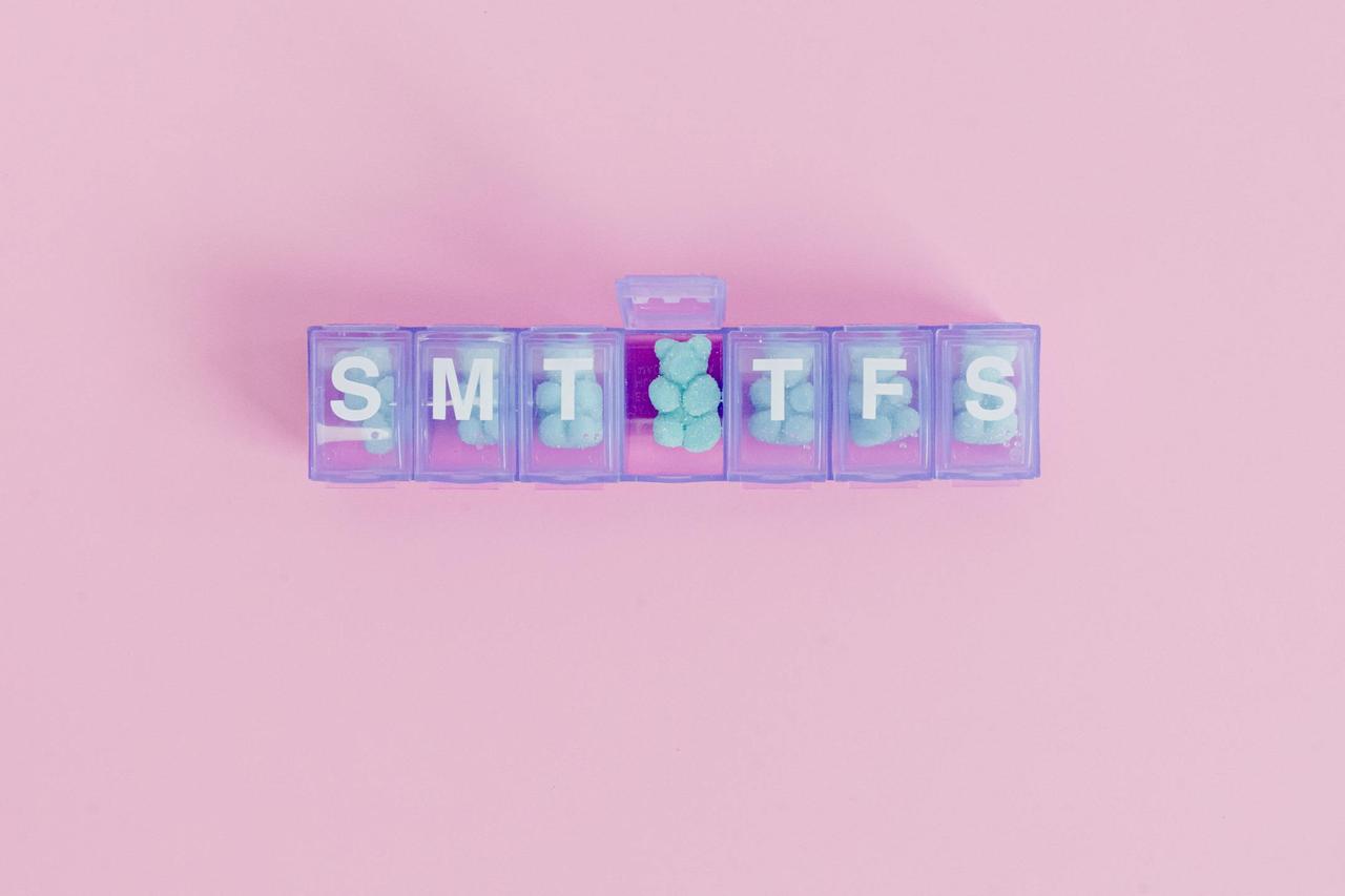 Top view of a weekly pill organizer filled with pills on a pink background.