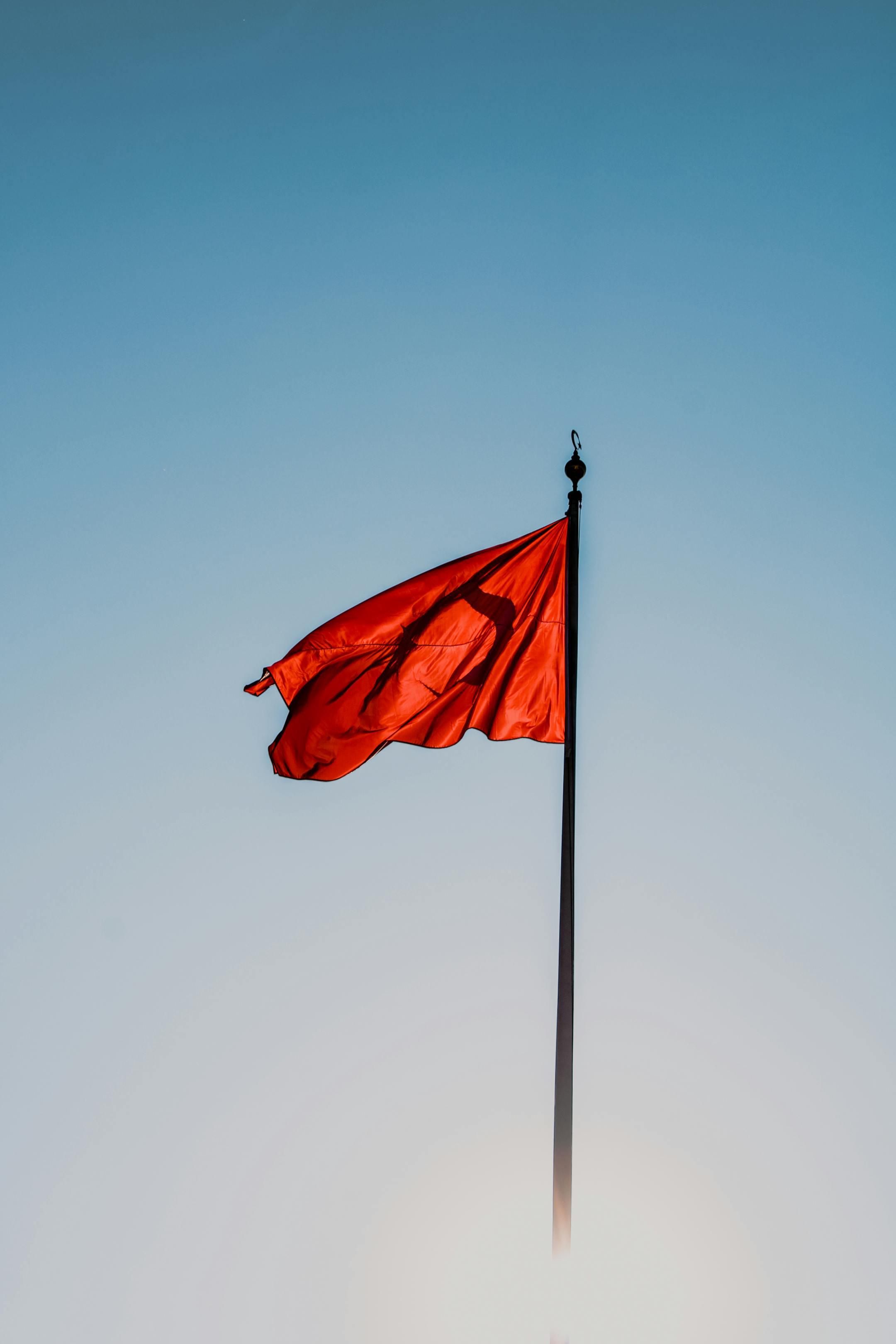A vibrant red flag waves against a clear blue sky on a tall flagpole in Türkiye.