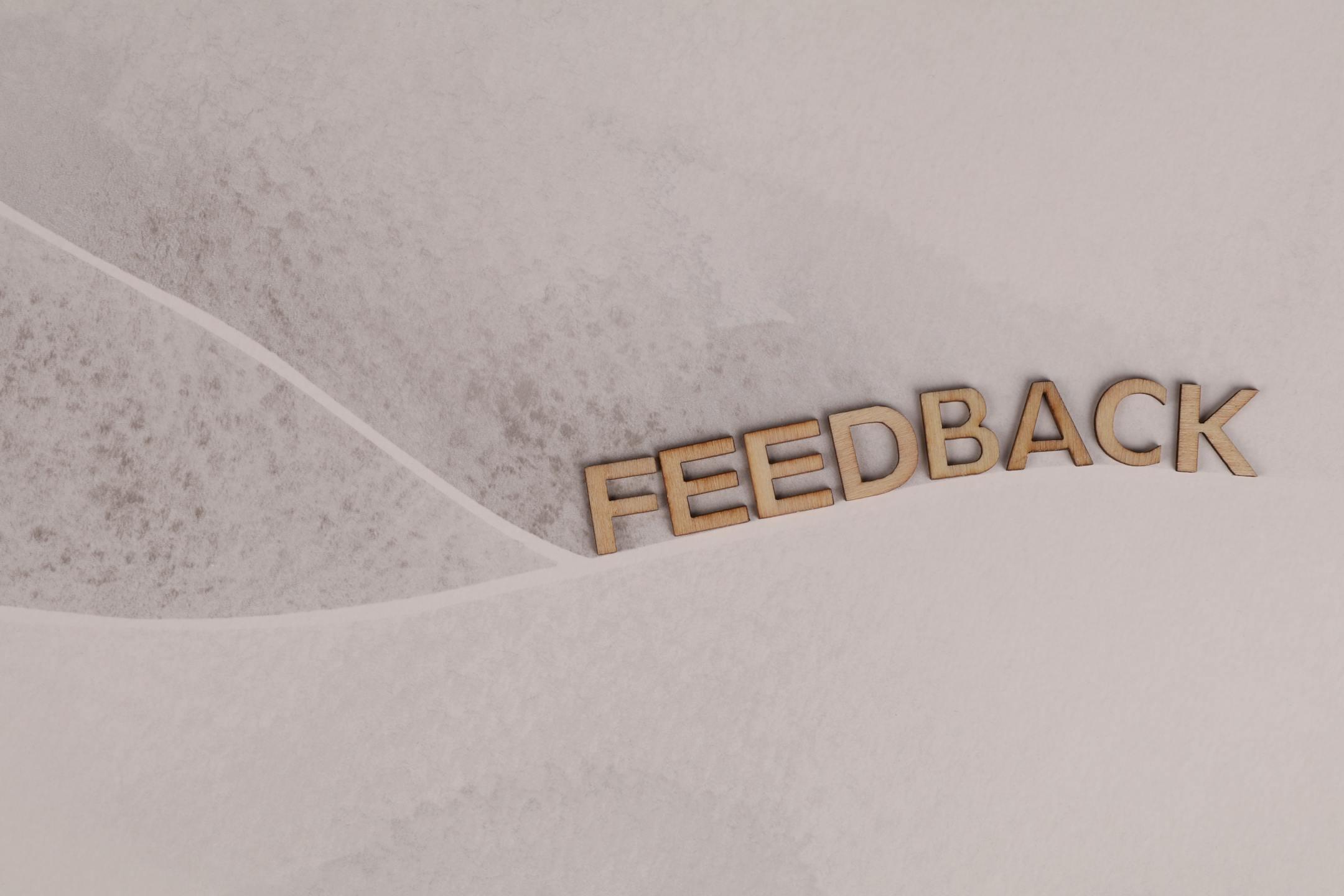 Wooden letters spelling 'FEEDBACK' arranged on textured paper background, conveying a conceptual theme.
