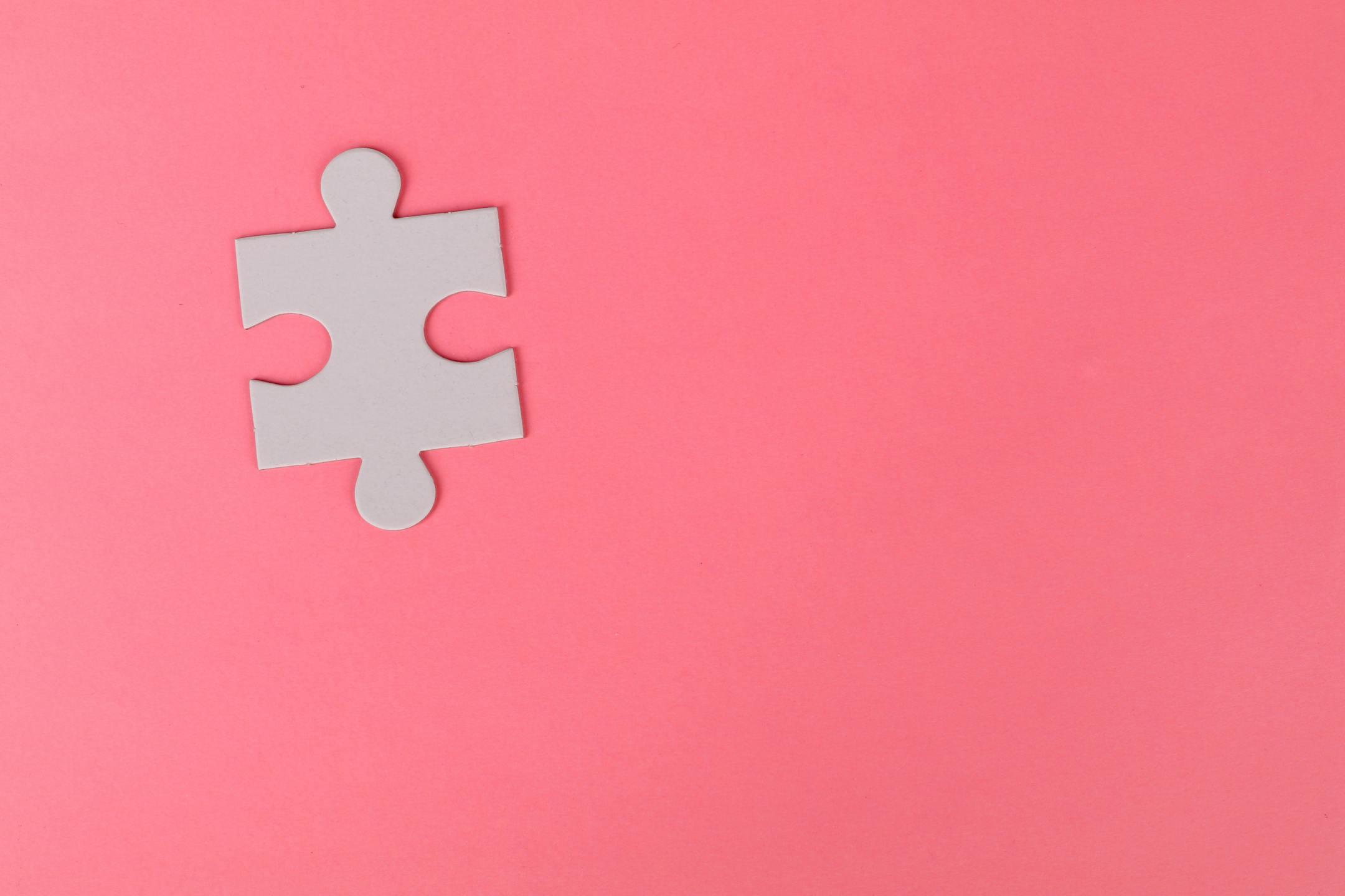 A single puzzle piece set against a vibrant pink background, offering ample copy space.