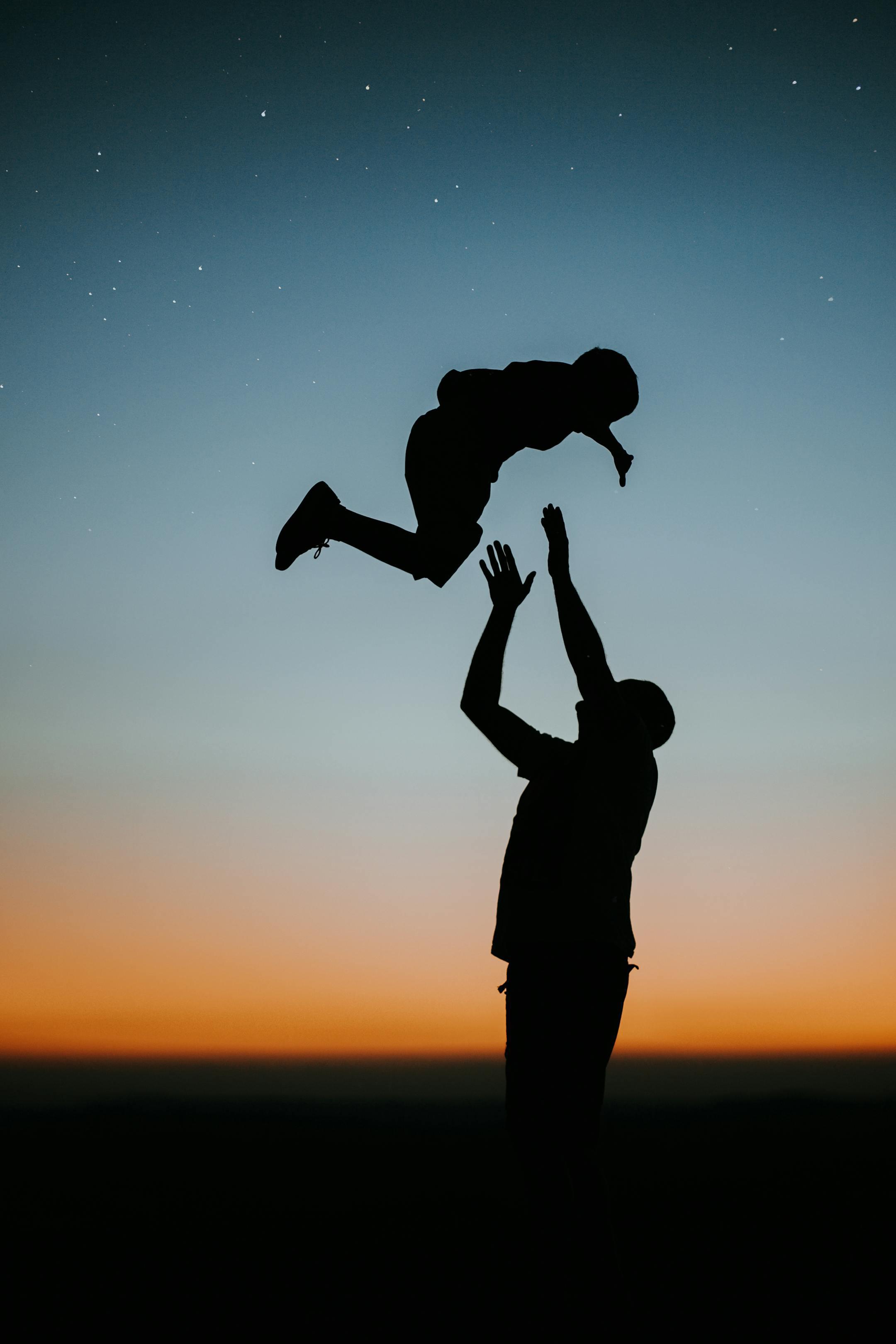 A father plays with his son at twilight, creating a joyous silhouette against the sunset sky.