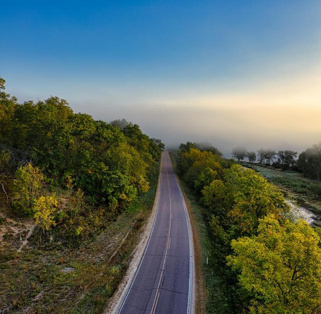 A serene aerial view of a foggy rural road in Wisconsin surrounded by autumn foliage.