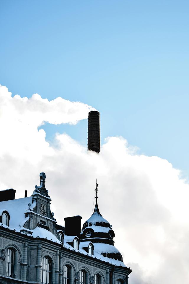 Snow-covered rooftop with chimney emitting smoke against a clear blue sky in Tampere, Finland.