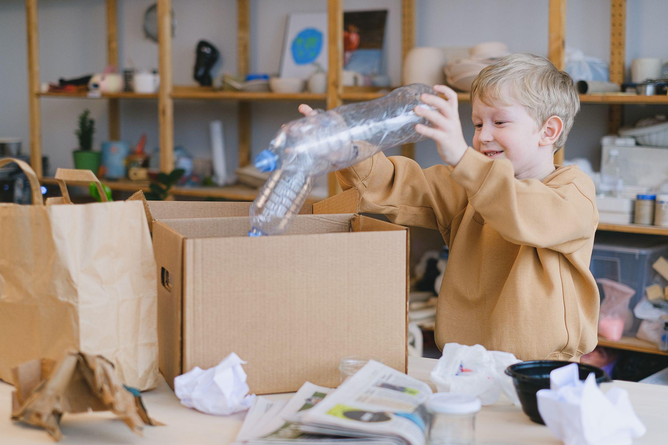 A young boy happily sorts plastic bottles into a cardboard box for recycling.