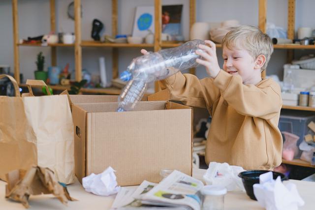 A young boy happily sorts plastic bottles into a cardboard box for recycling.