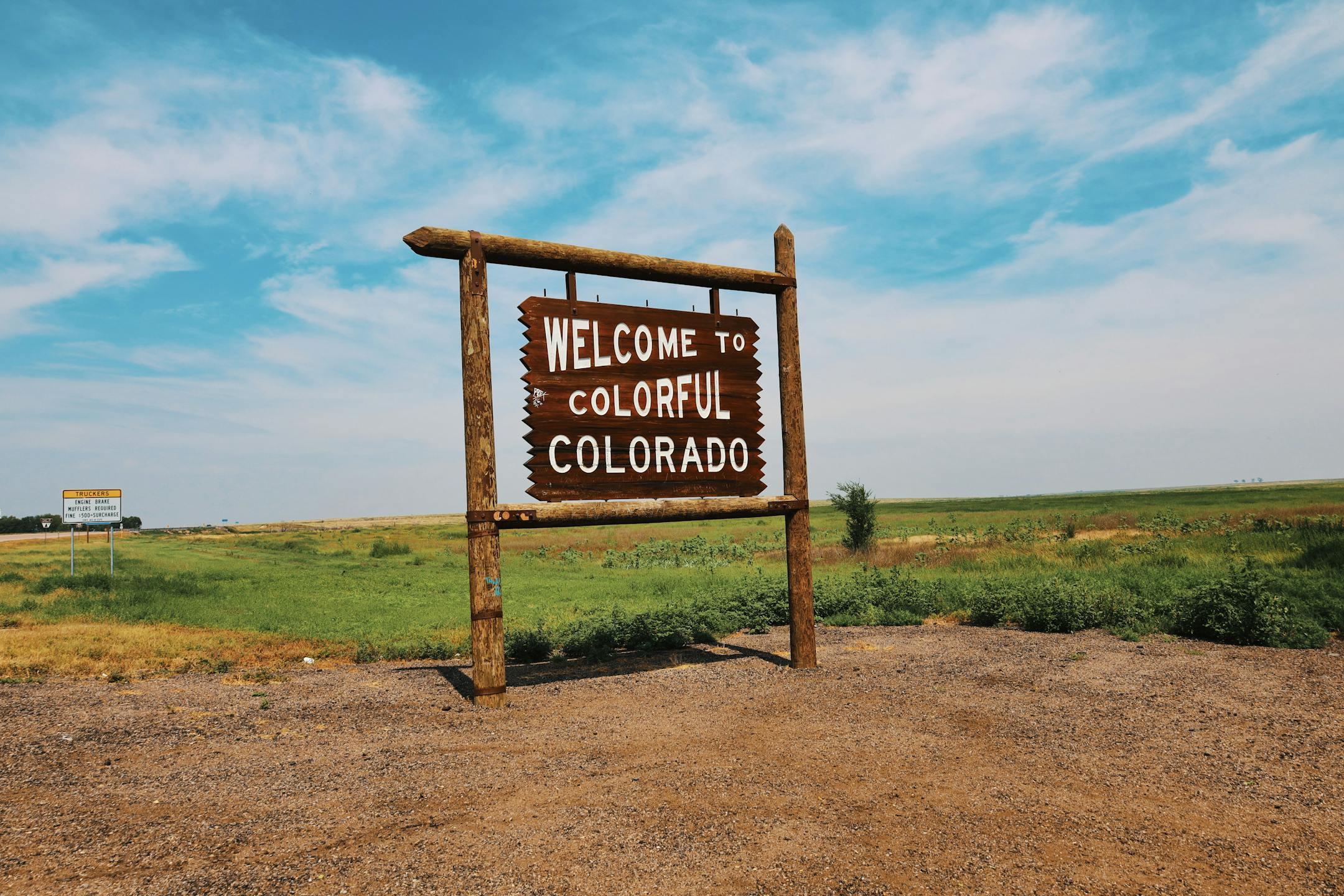 Wooden welcome sign in a Colorado field under a bright, clear sky.