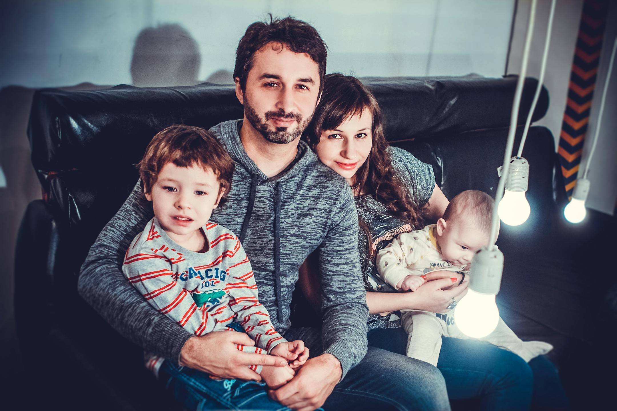 A joyful family of four sitting on a sofa, smiling warmly indoors.