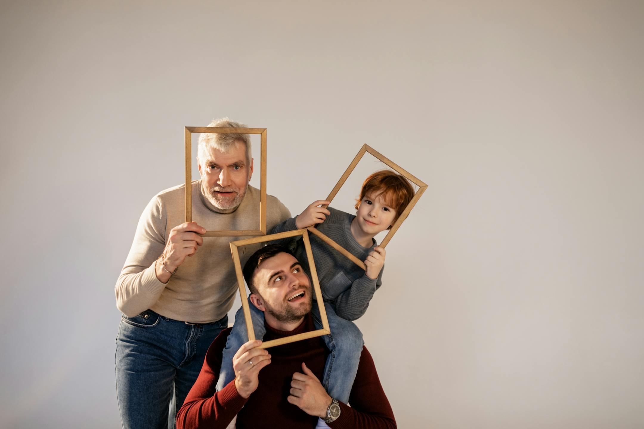 A joyful family portrait featuring grandfather, dad, and child posing with wooden frames in a studio setting.
