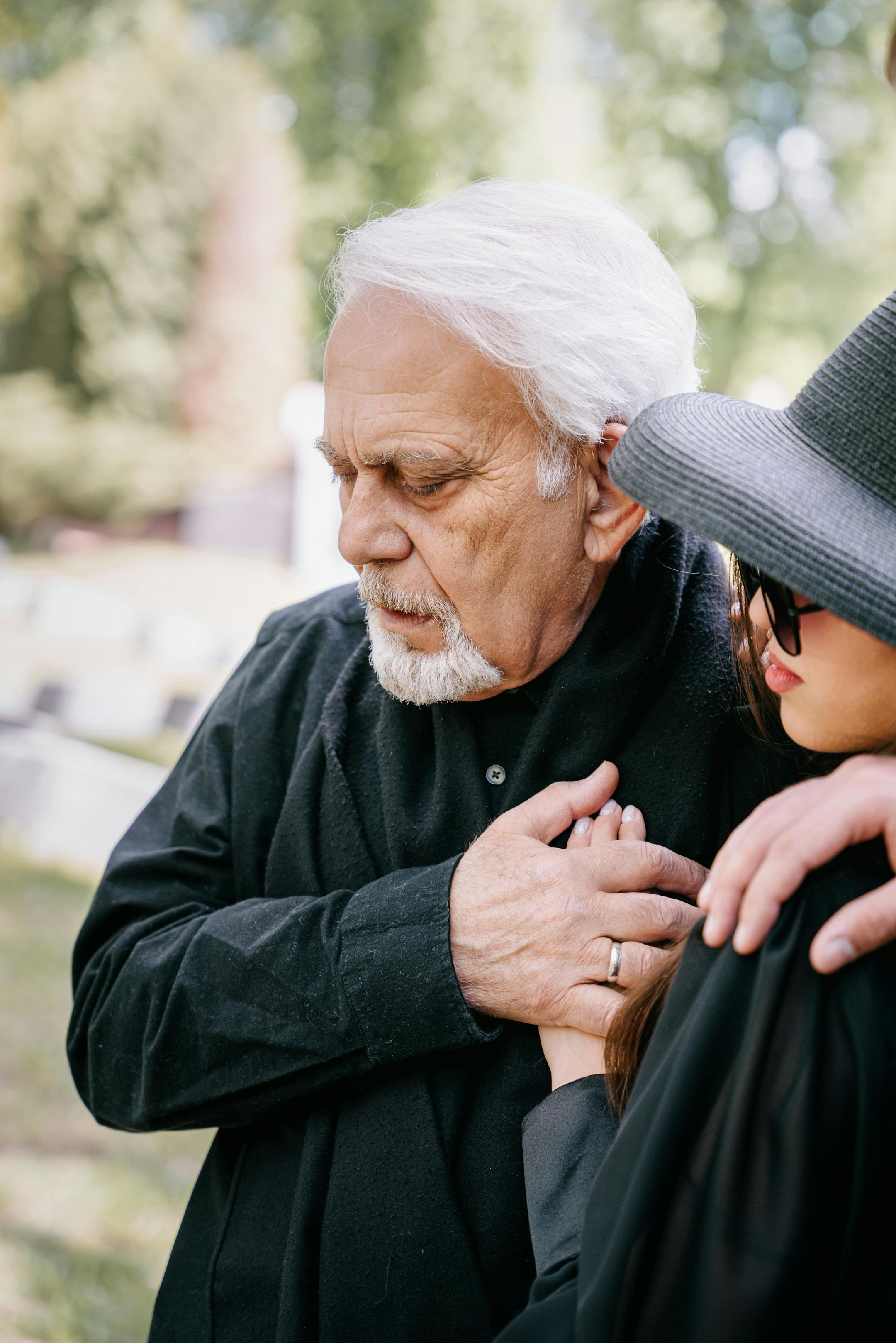An elderly man and woman share a heartfelt moment at a cemetery,signifying loss and togetherness.