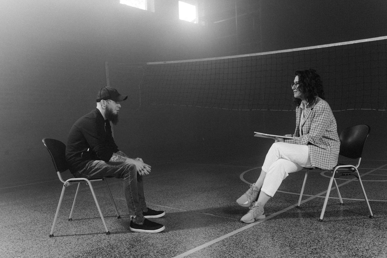 Black and white photo of therapy session between bearded man and counselor in gym.