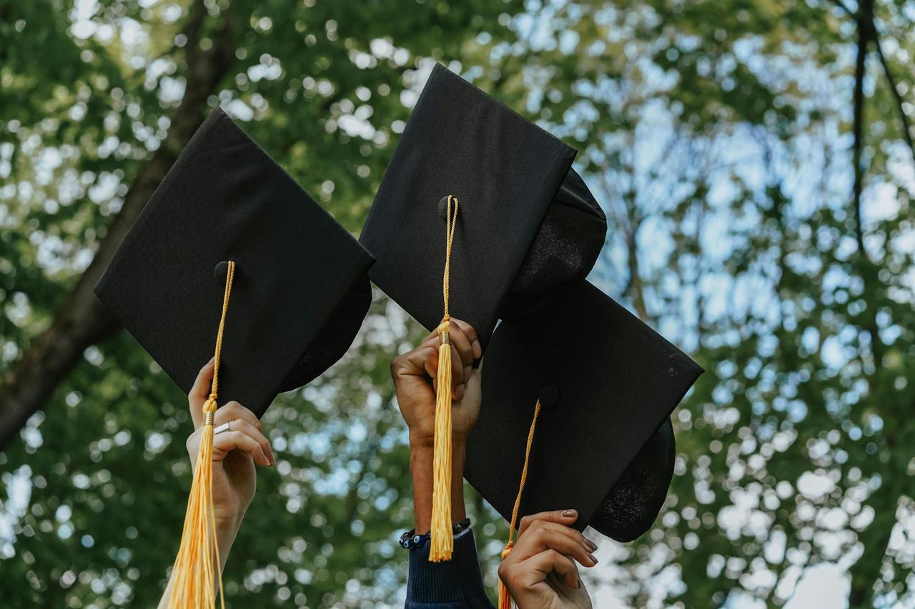 Three hands holding graduation caps in celebration, symbolizing success.