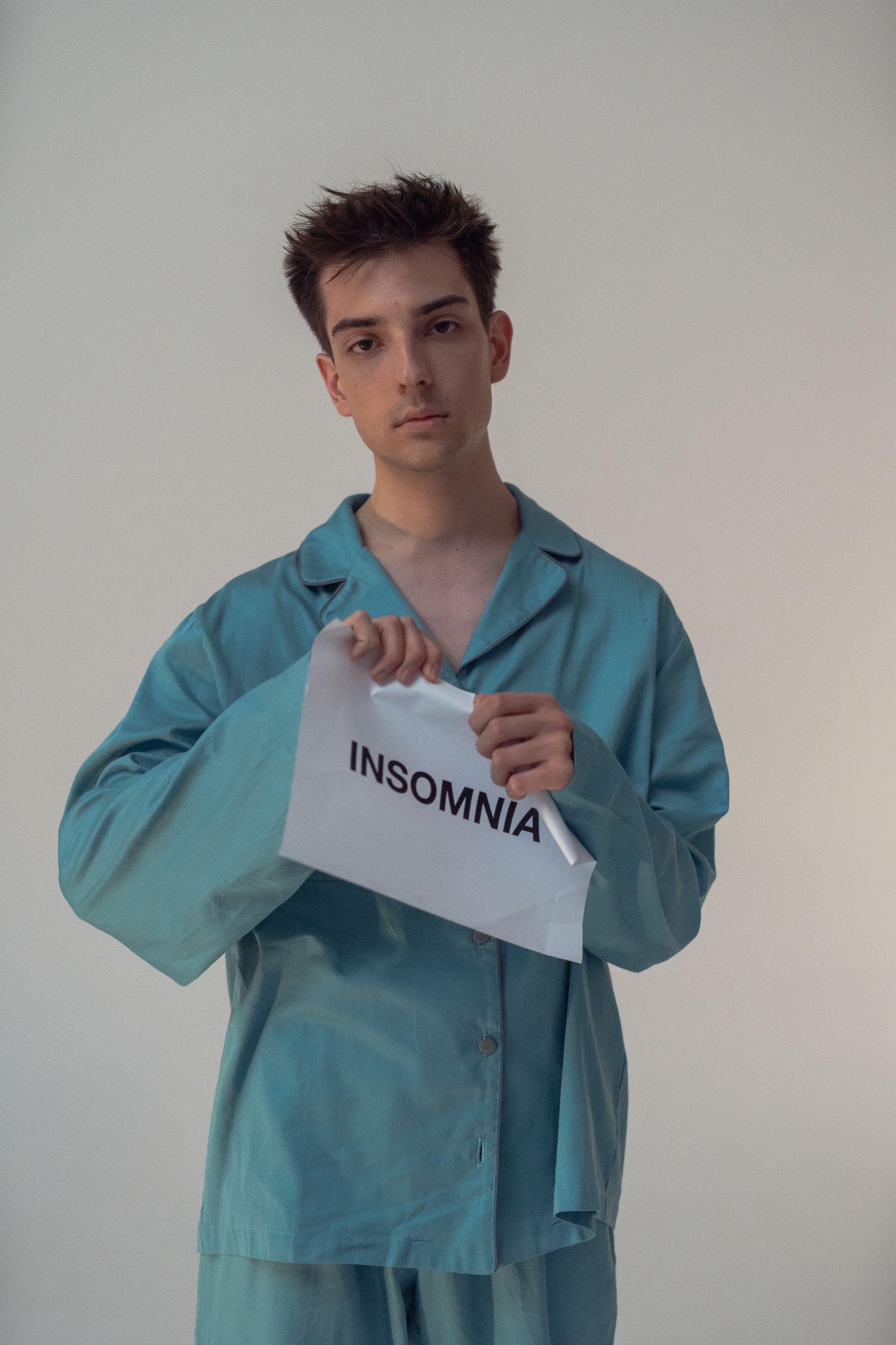 Young man in pajamas holding a sign reading 'Insomnia,' highlighting sleep disorders.