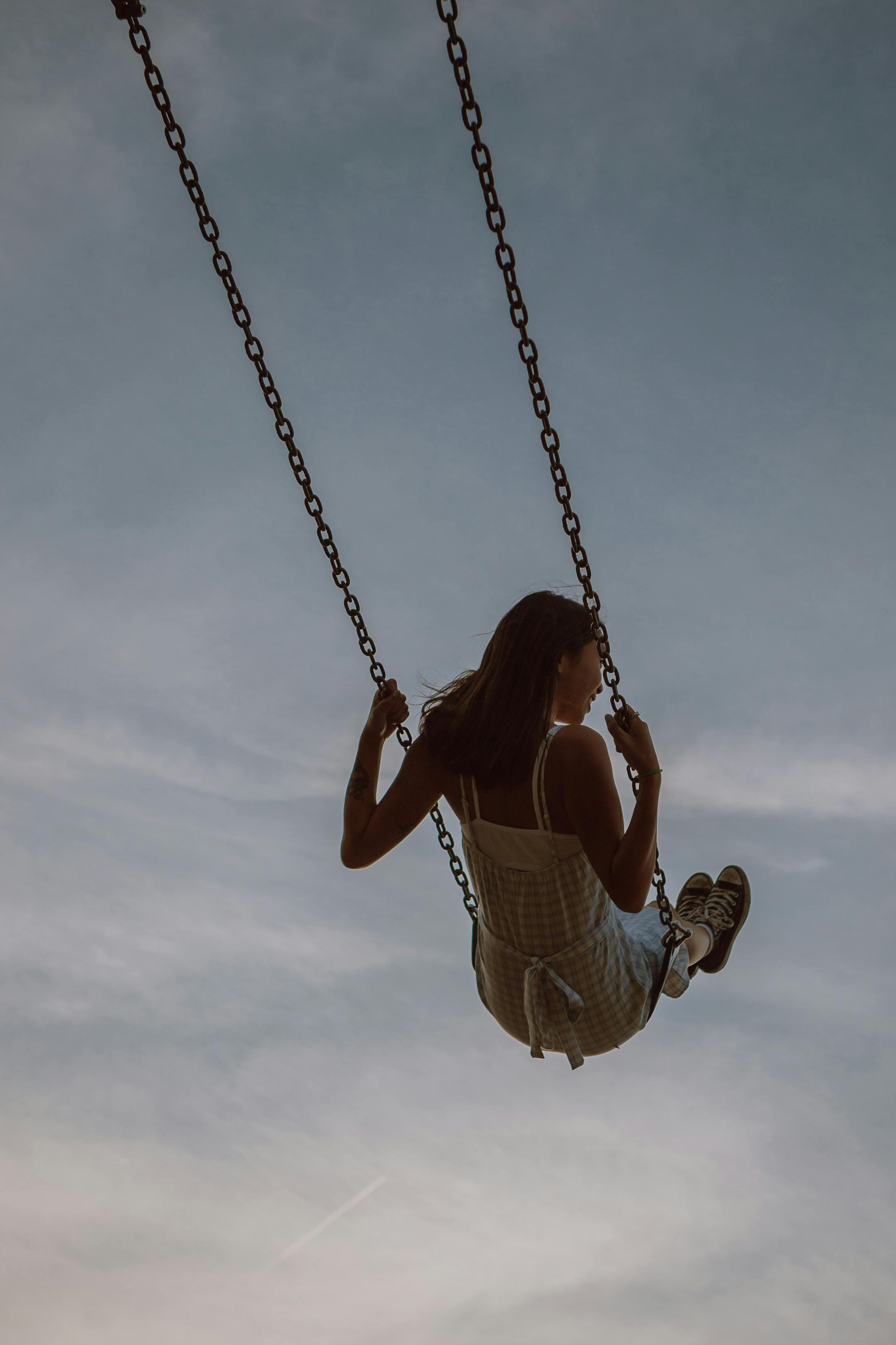 A young woman enjoying a carefree moment on a swing with a serene sky backdrop.