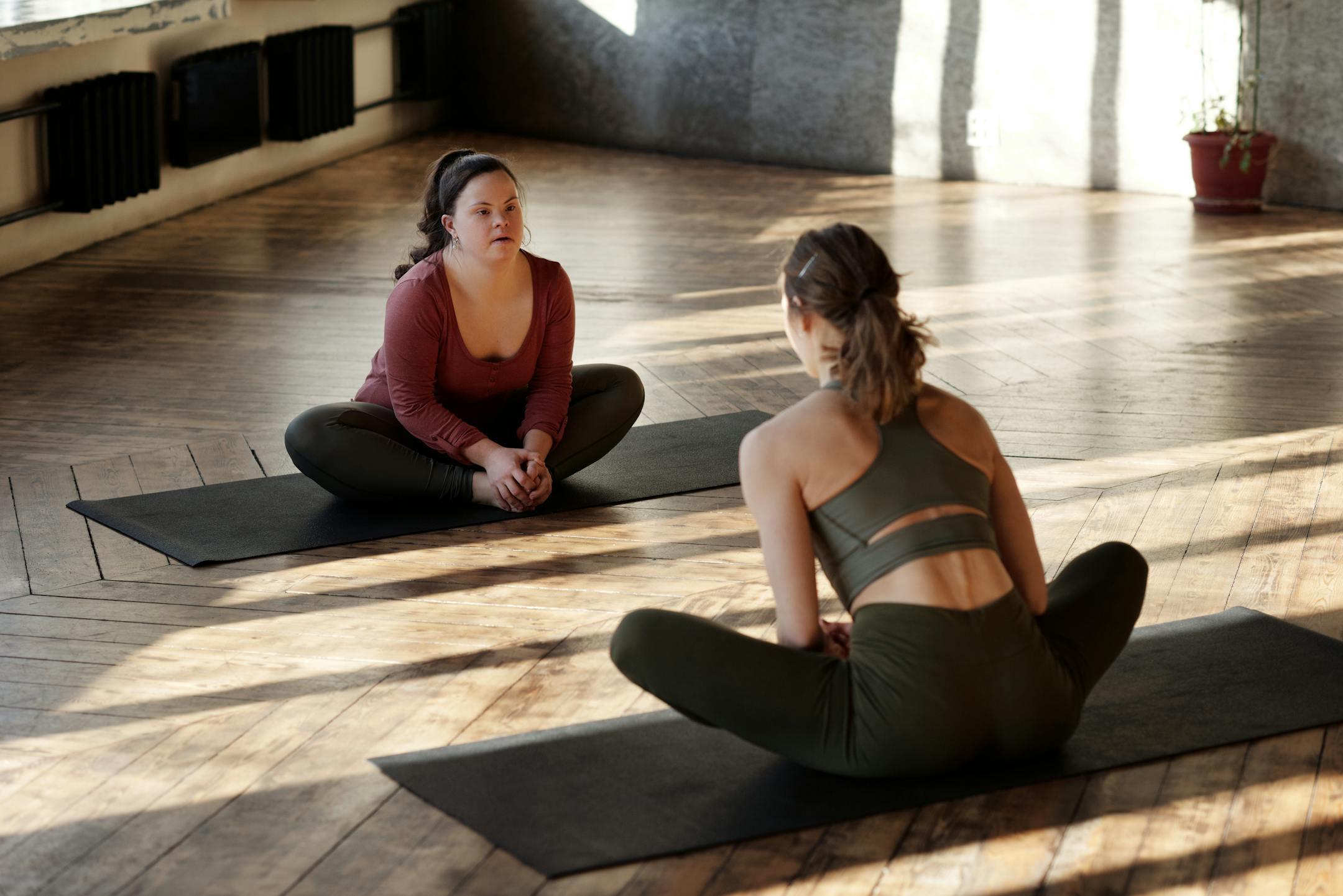 Two women practicing yoga indoors, embracing diversity and wellness.