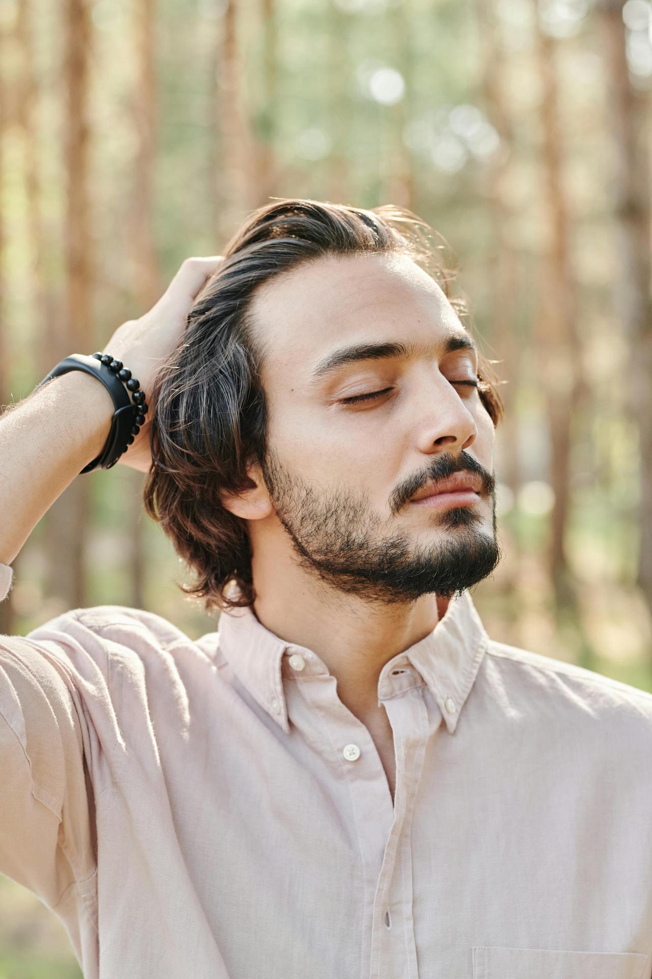 Portrait of a serene young man with closed eyes, enjoying nature in a sunlit forest setting.