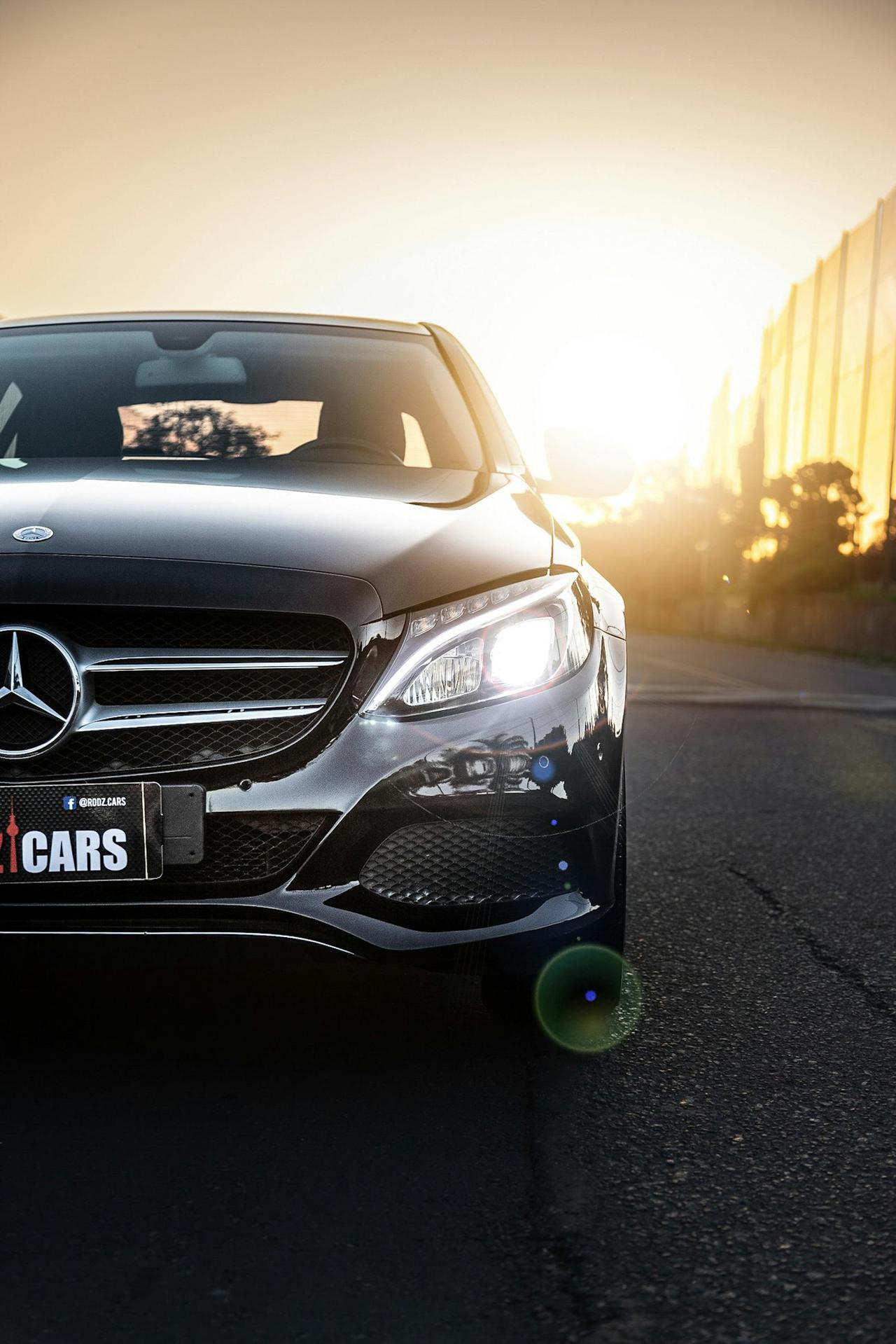 Front view of a parked Mercedes-Benz C180 during a beautiful sunset with glowing headlights.