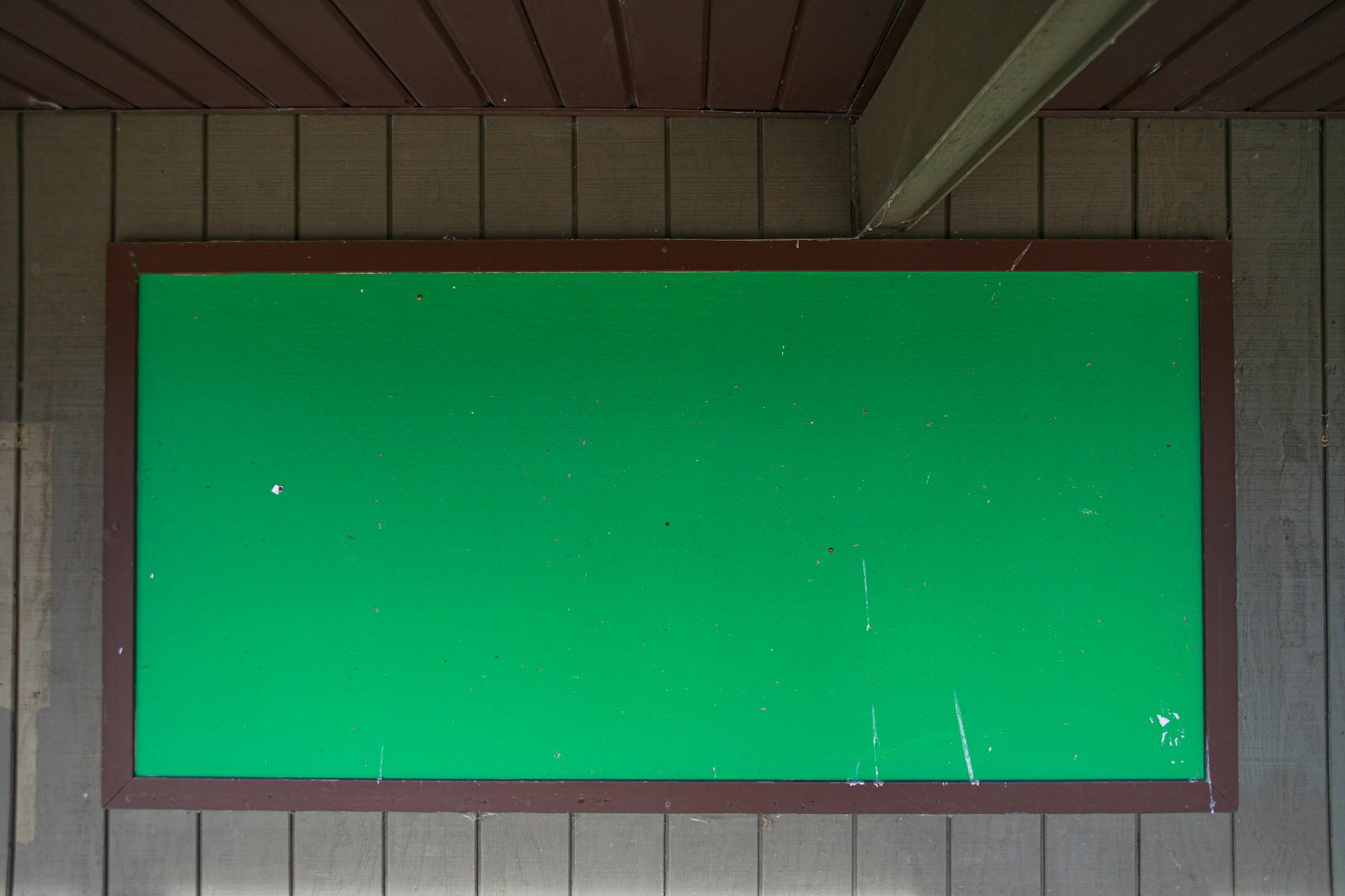 A bright green message board is mounted to the outside of a park wall. 