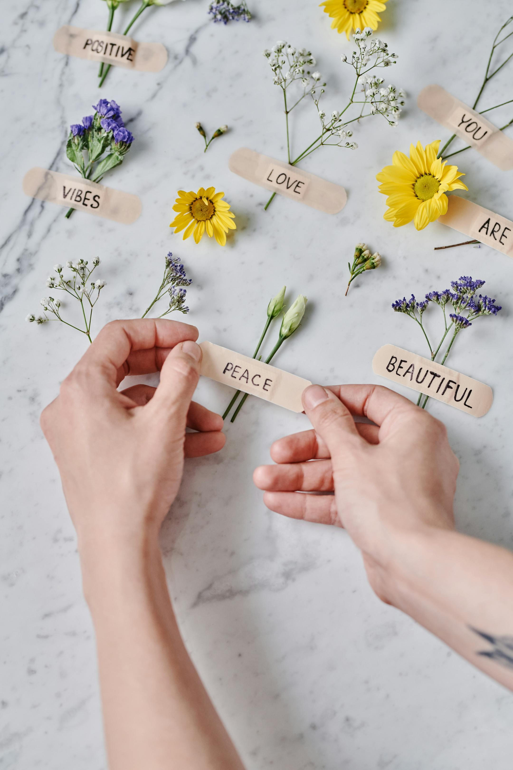 Hands arranging flowers with positive words on bandages for a creative and uplifting display.