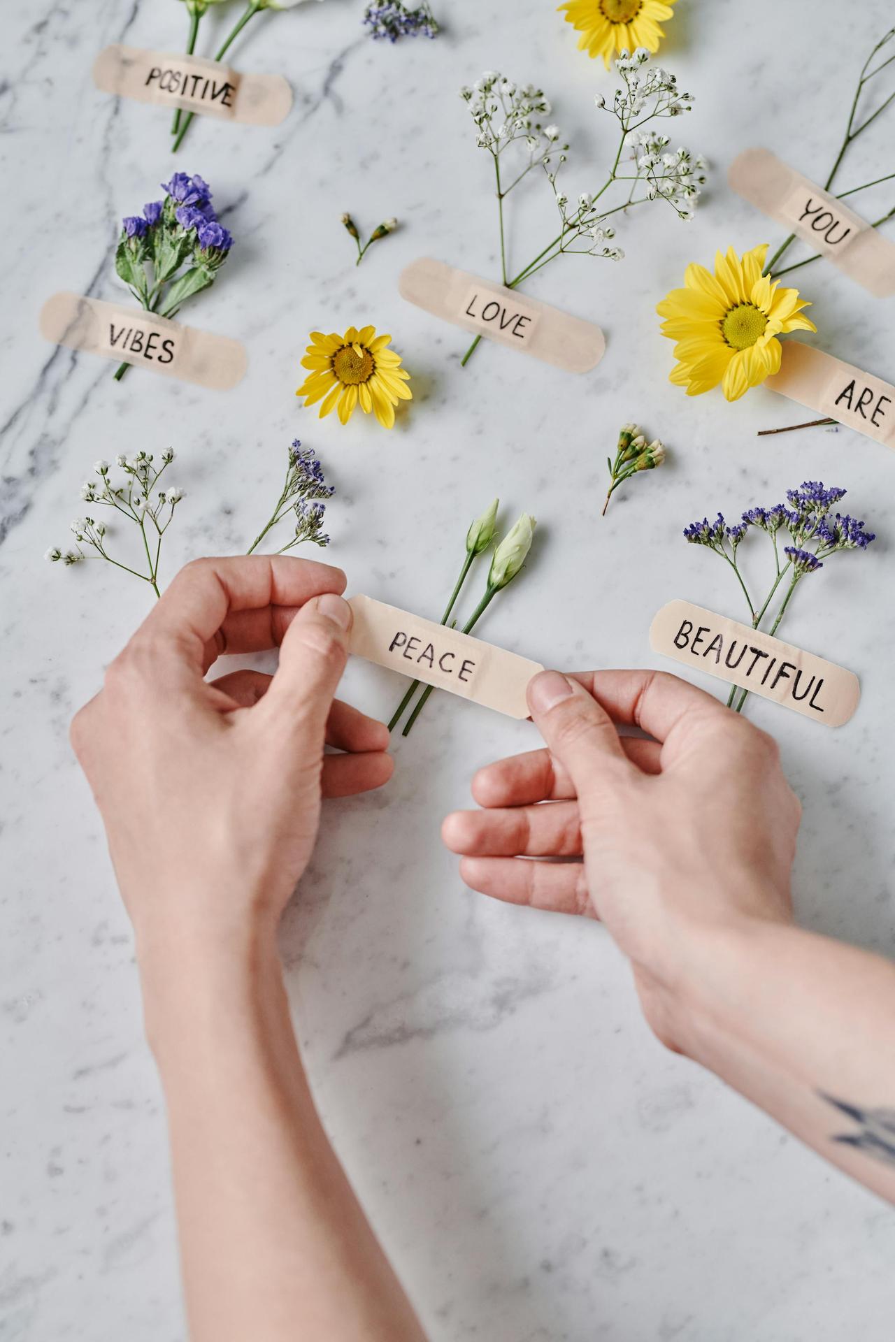 Hands arranging flowers with positive words on bandages for a creative and uplifting display.