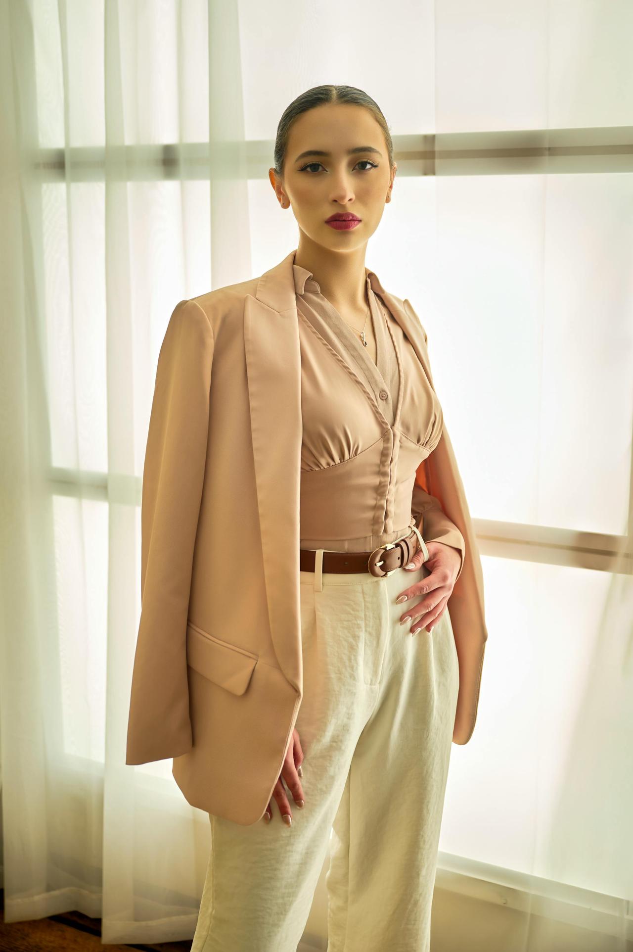 Young woman posing confidently in chic neutral clothing indoors with natural light.